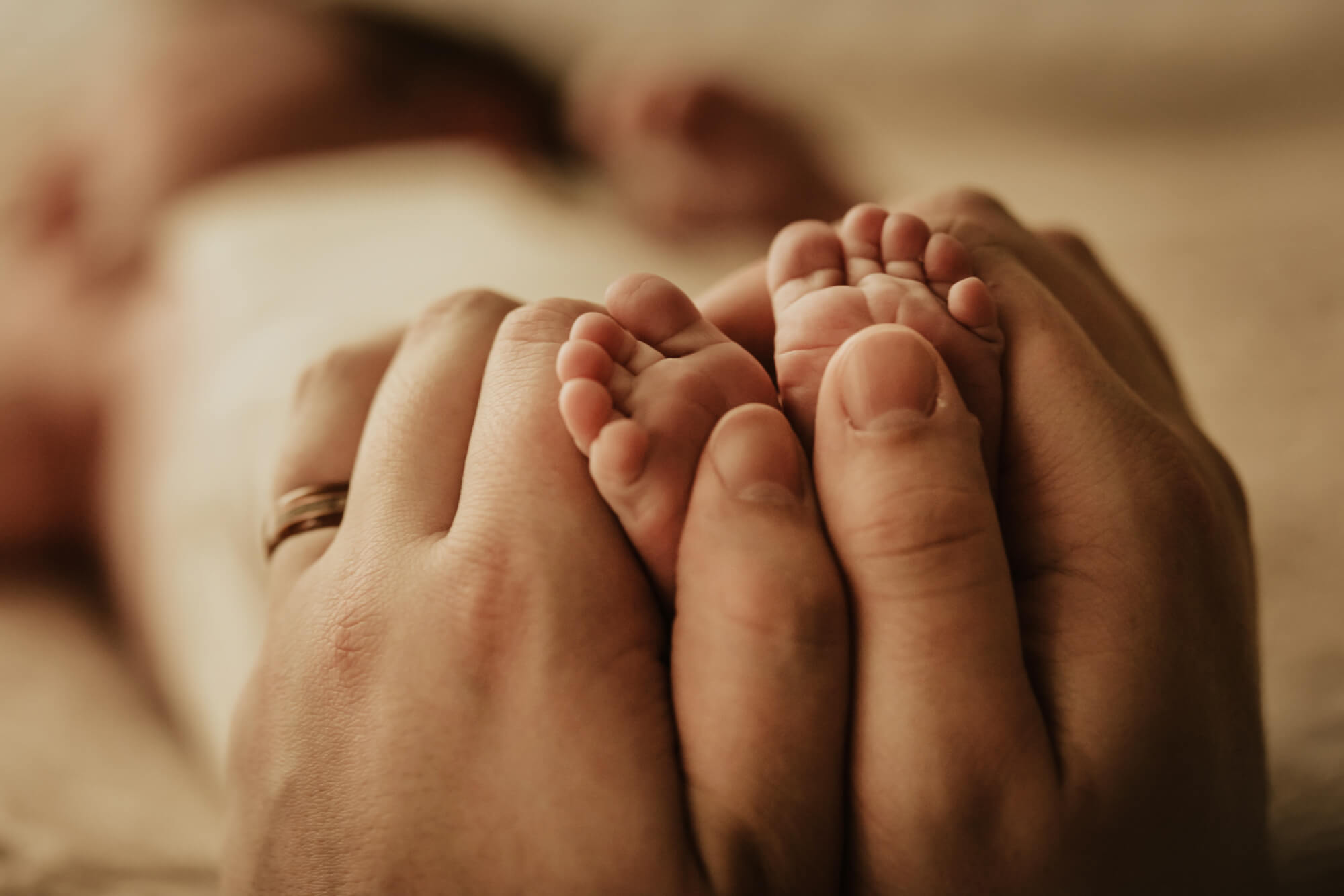 Details of a father holding his newborn baby's feet while they sleep beautifully connected