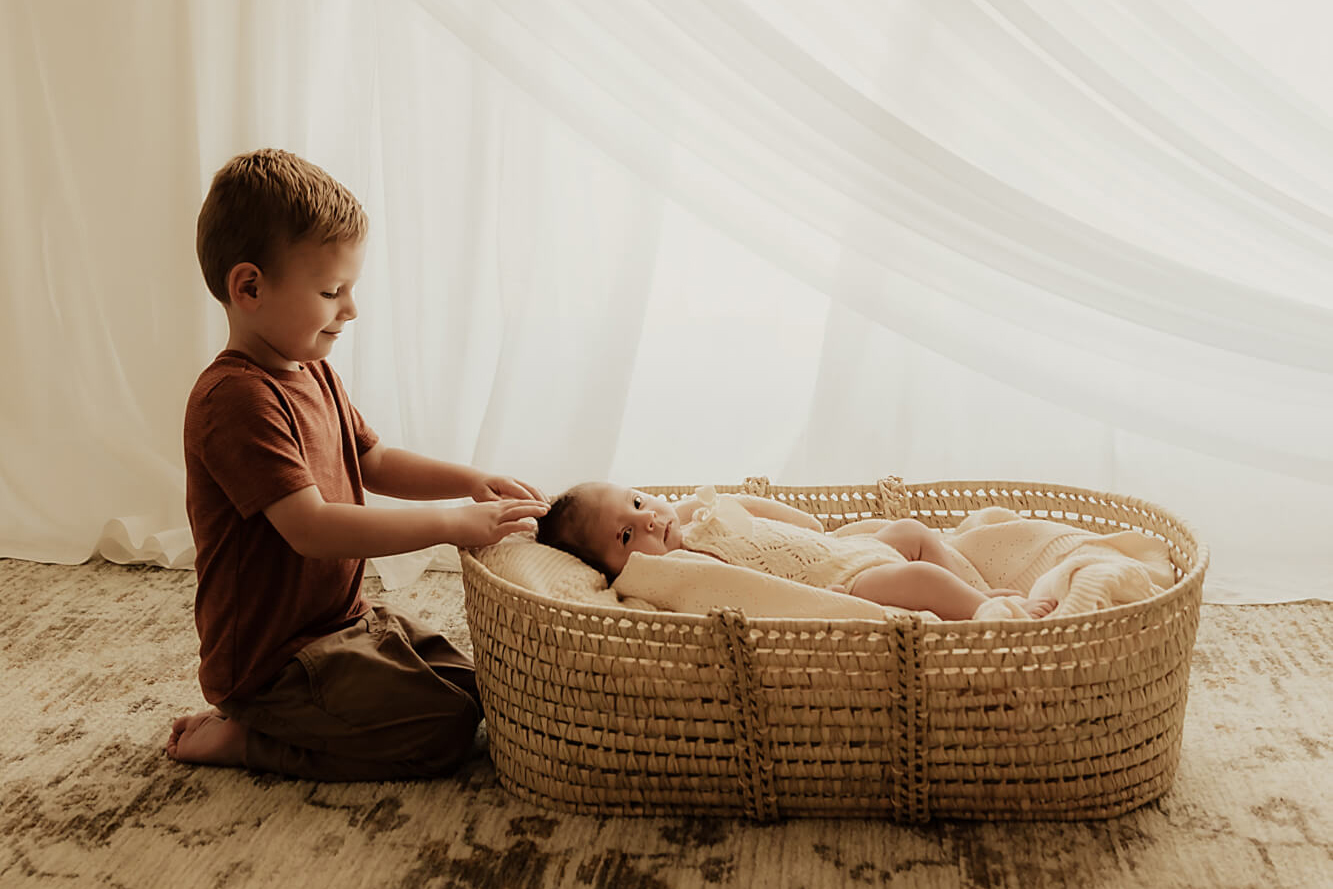 Little boy looking down at his newborn baby sister in a basket, natural okie baby.