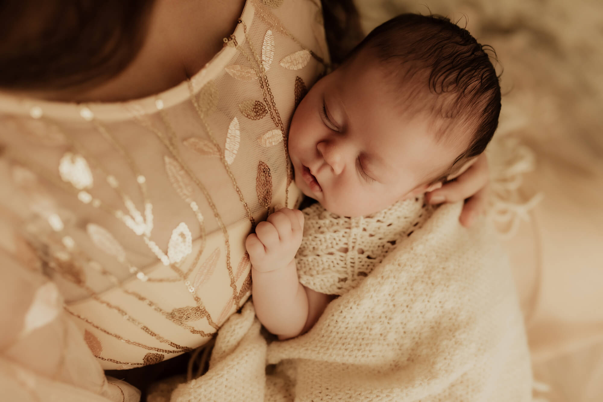 A newborn baby sleeps against mom's chest in a knit onesie