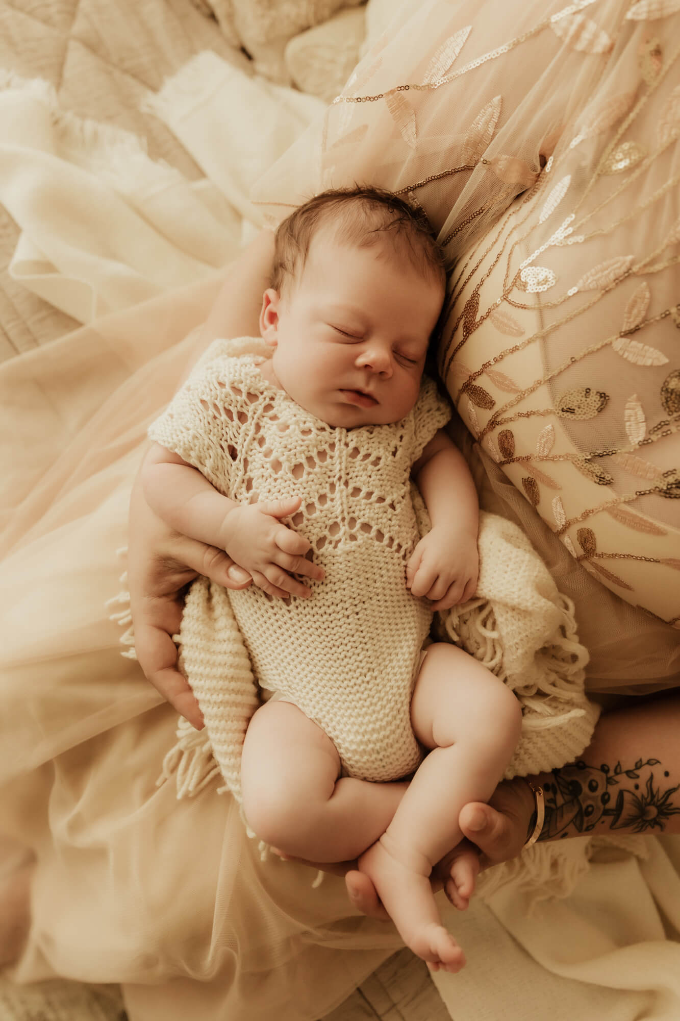 A newborn baby sleeps in a knit onesie in mom's lap
