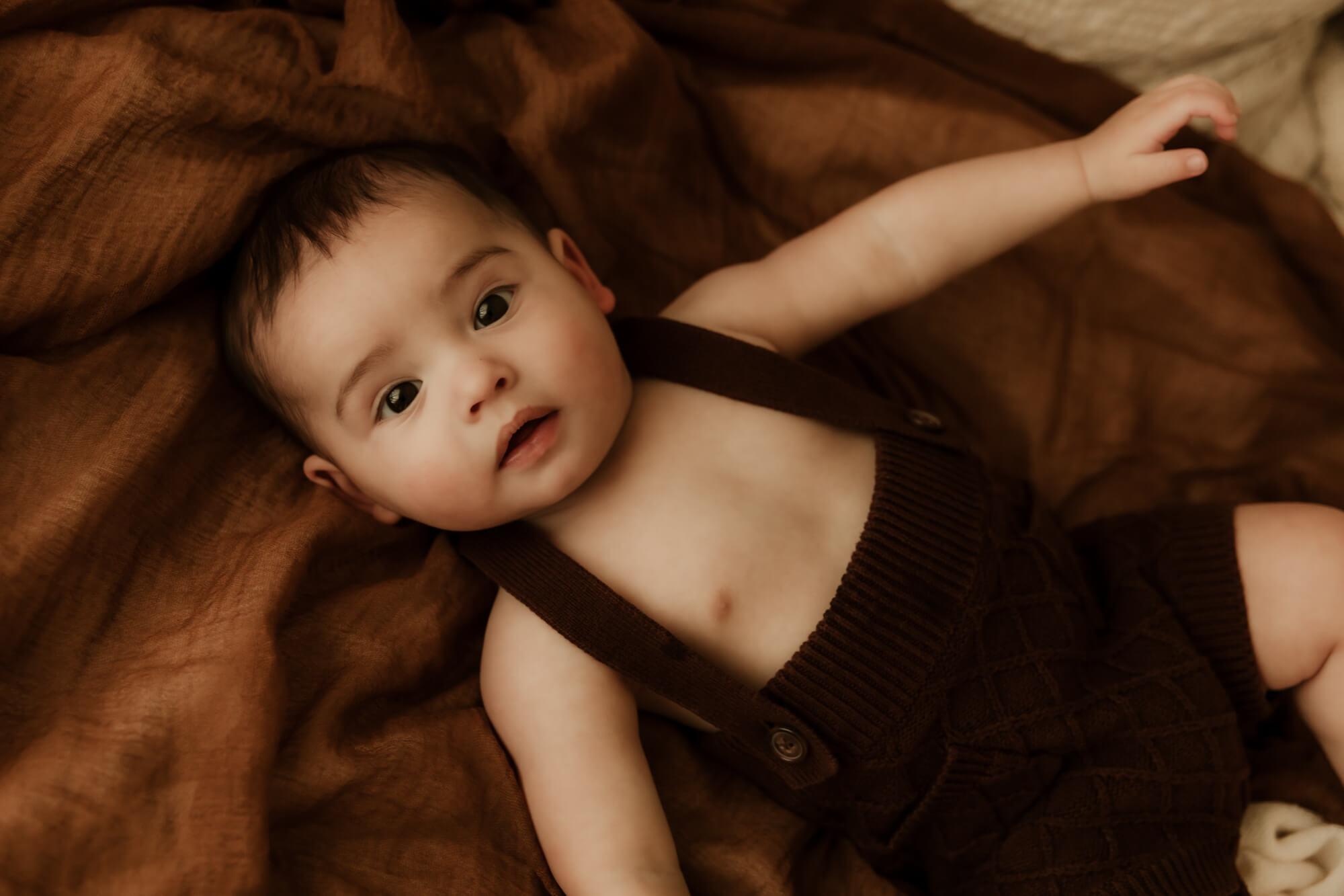 Little boy laying on his back while wearing a brown romper.