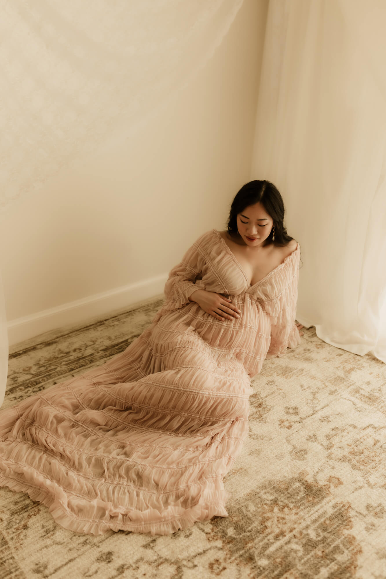 Mother sitting down on a rug posed for her maternity portrait, Miracle in the Womb.