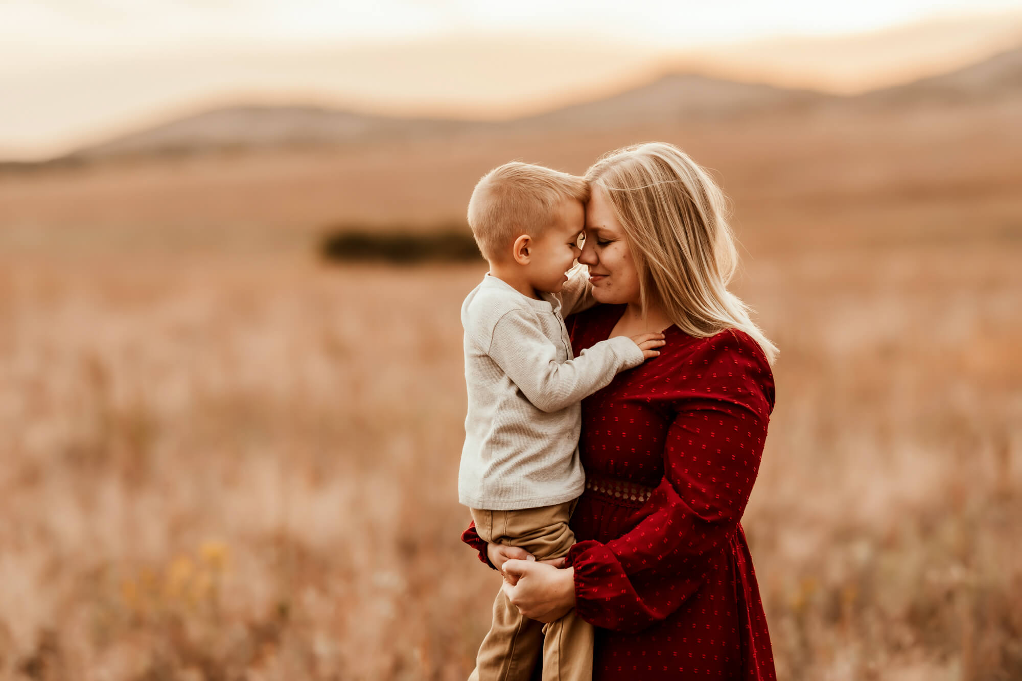 Mother snuggles her son in a field.