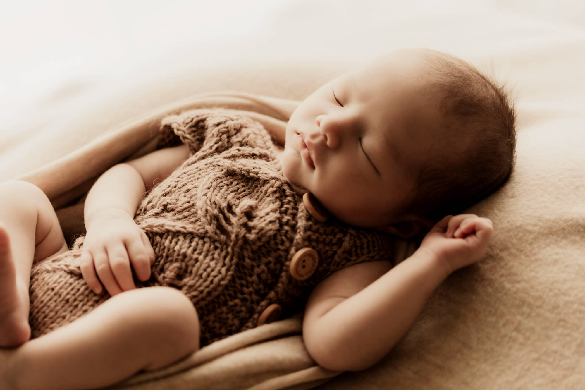 Baby wearing a brown knit romper sleeping, mosaic midwifery.