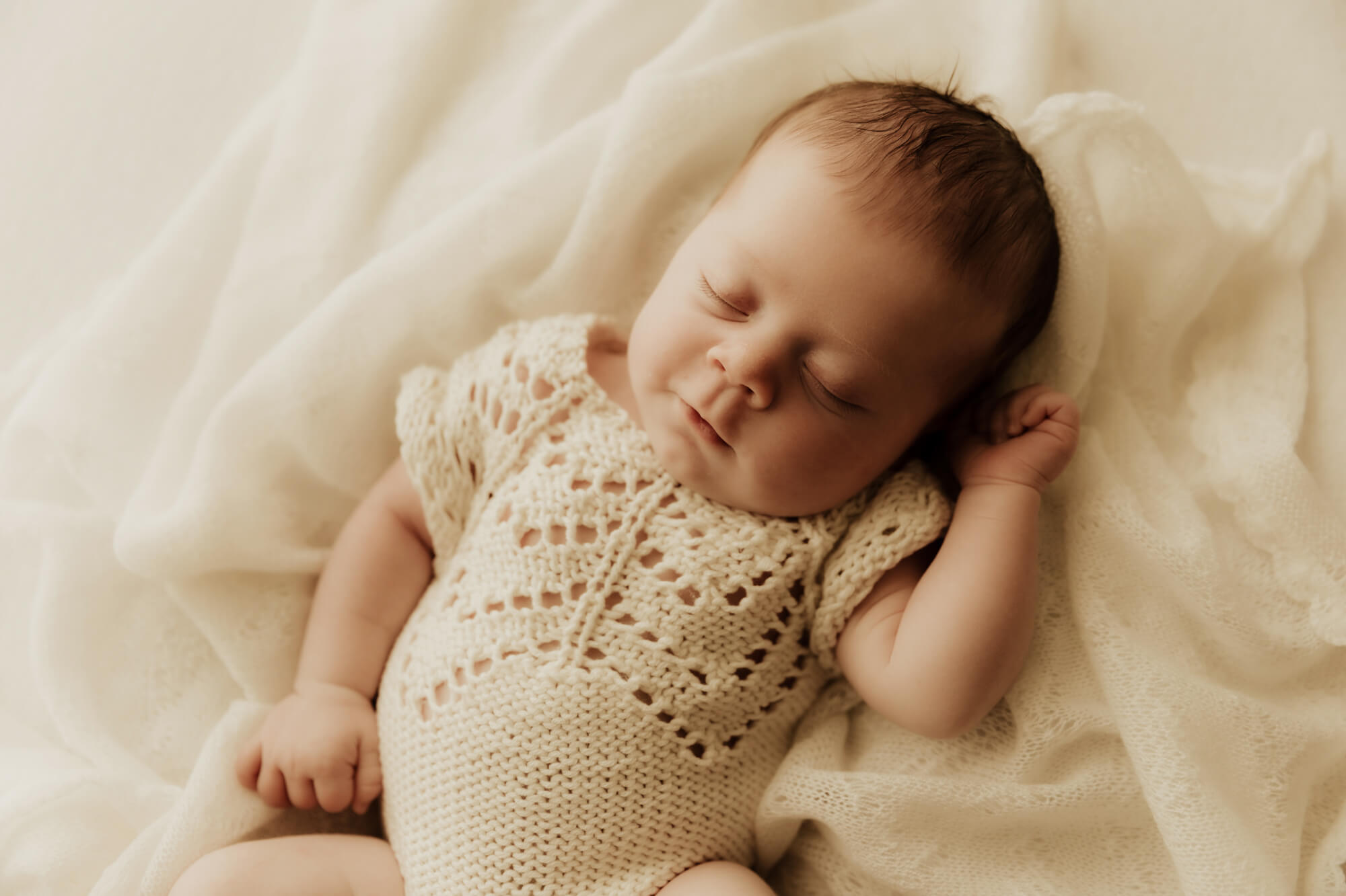 Newborn baby girl sleeping while wearing a cream colored knit romper.