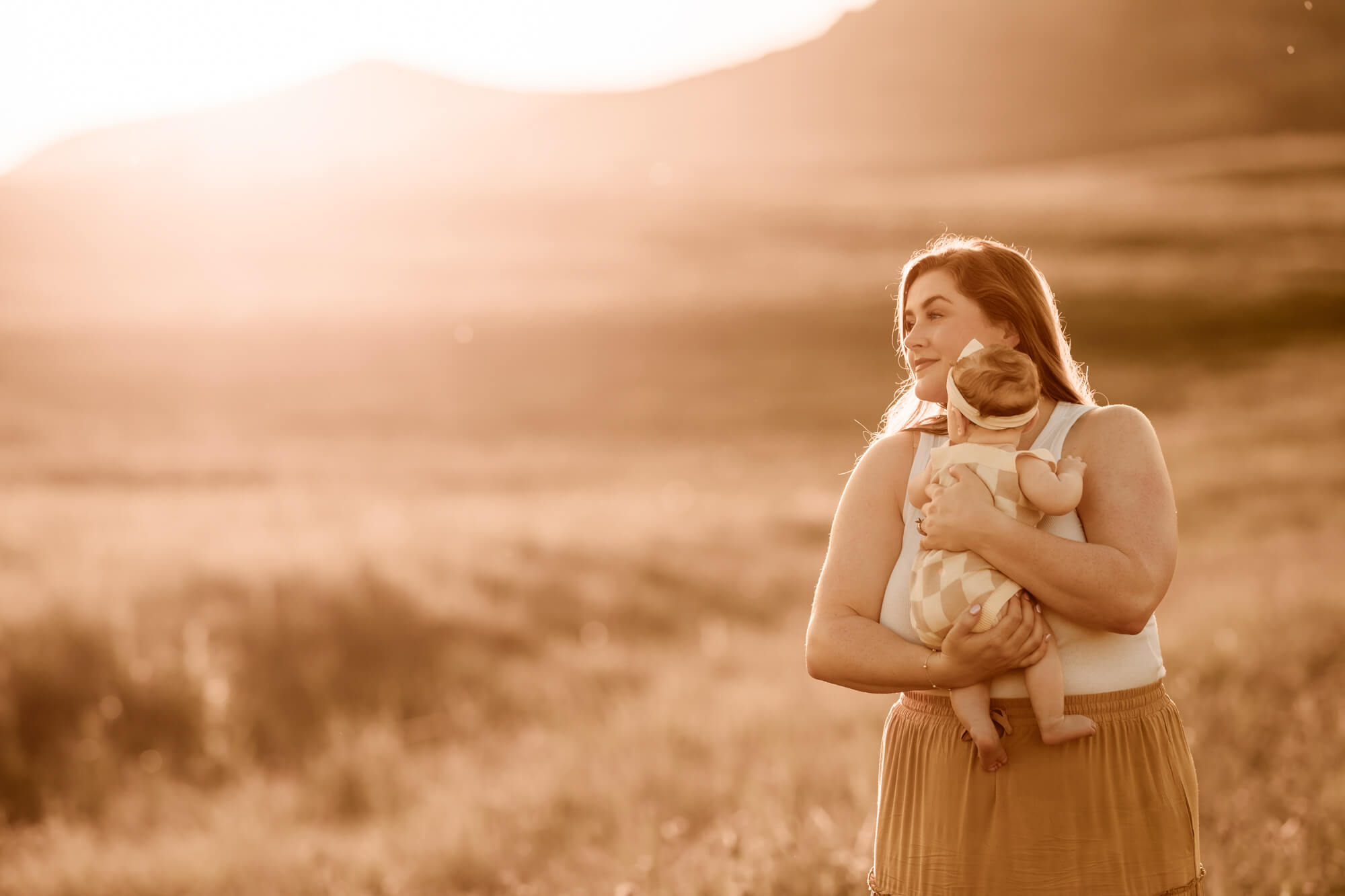 Mother holds her daughter near mountains in a field.