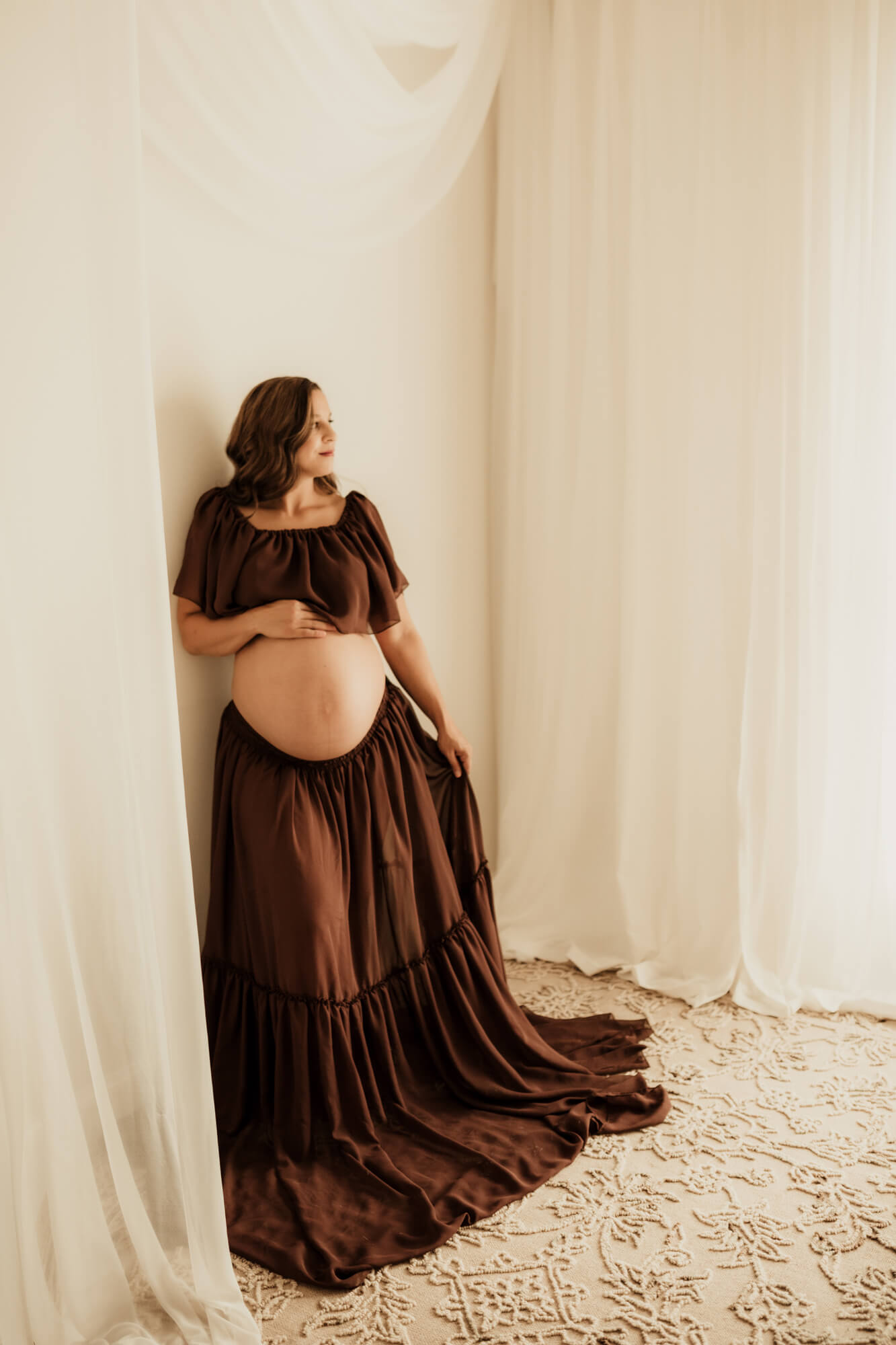Pregnancy portrait of mother wearing a brown two piece dress posed for a studio photo.