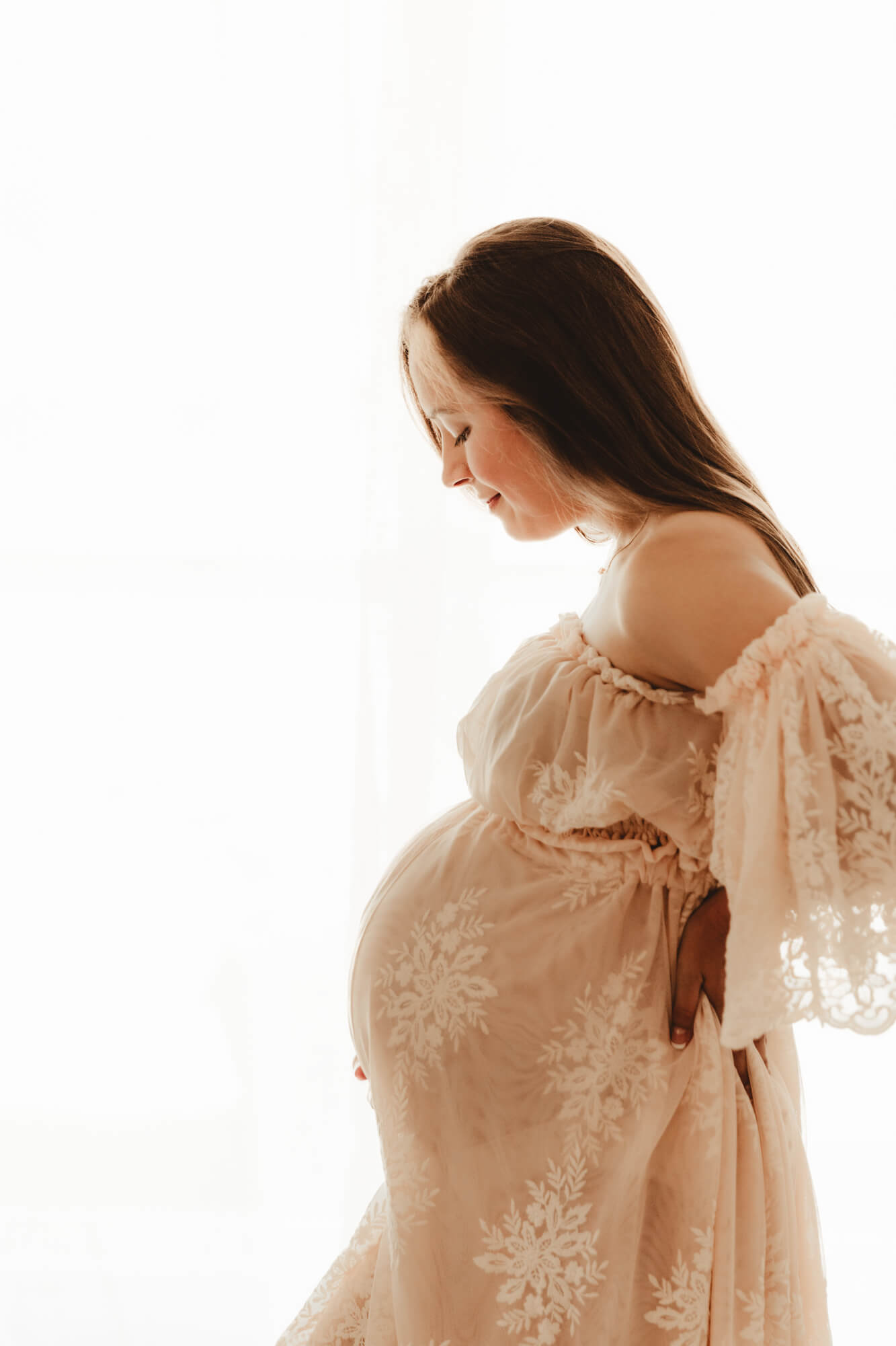 Pregnancy photo of woman wearing a blush lace dress and looking at her baby bump, Dr Goff OKC.