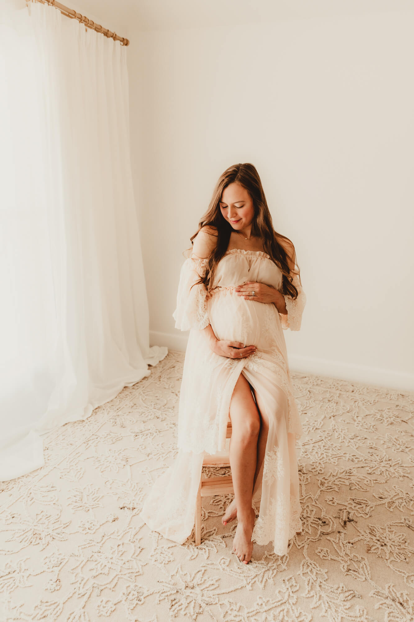 Woman sitting on a stool while looking down and her hands placed on her belly.