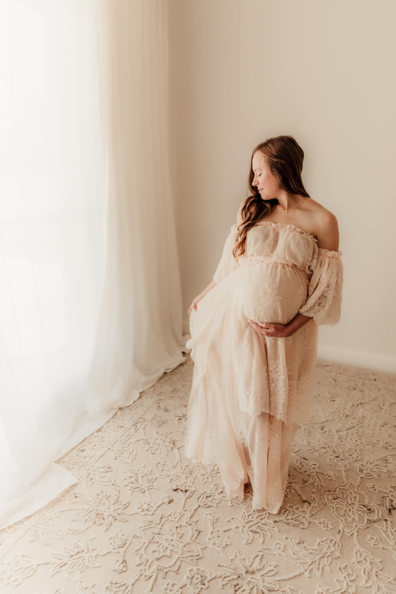 Woman holds her dress and her baby bump while looking down. 