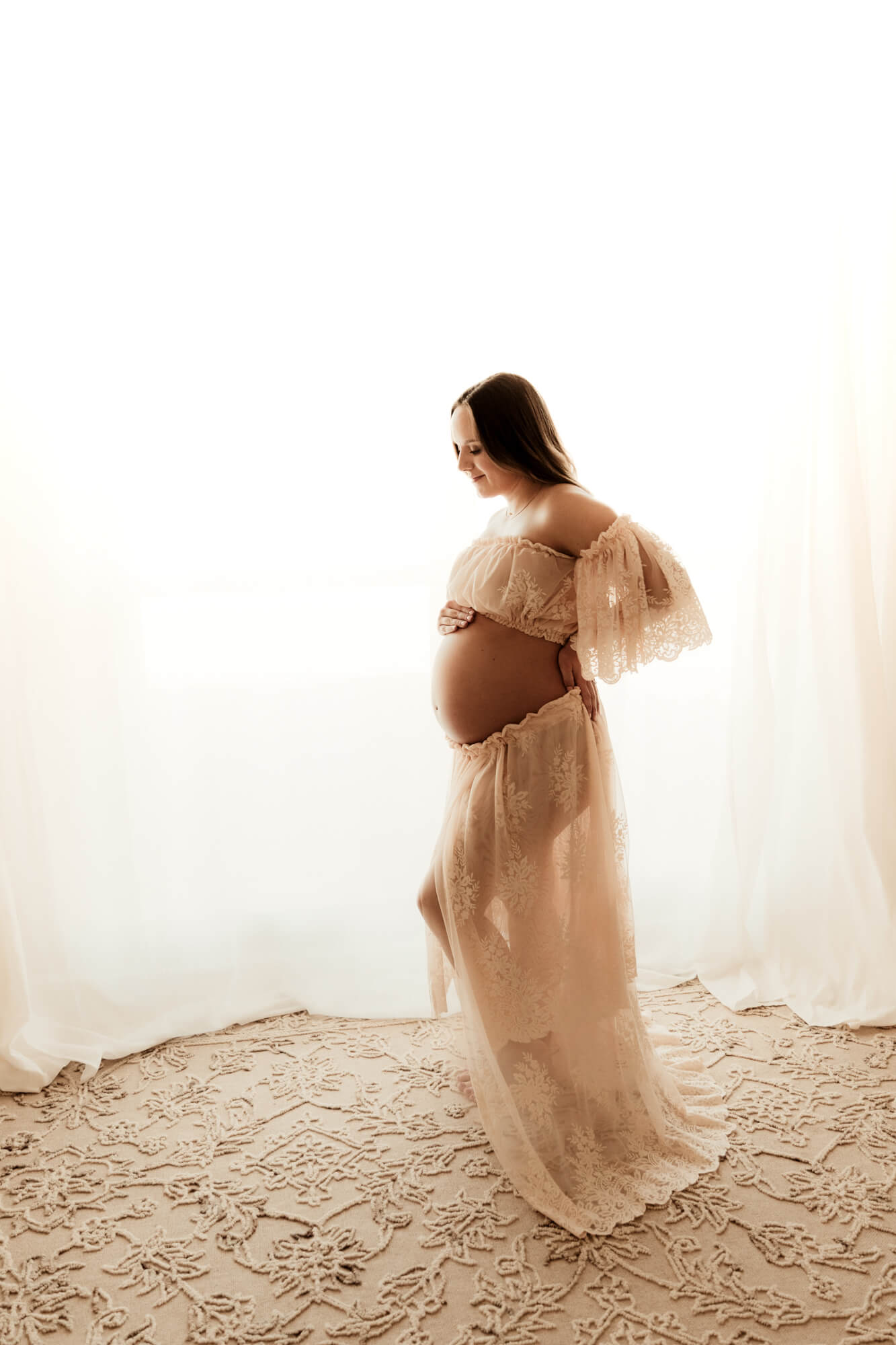 Maternity photo of a expecting mother holding her baby bump while wearing a two piece lace dress.