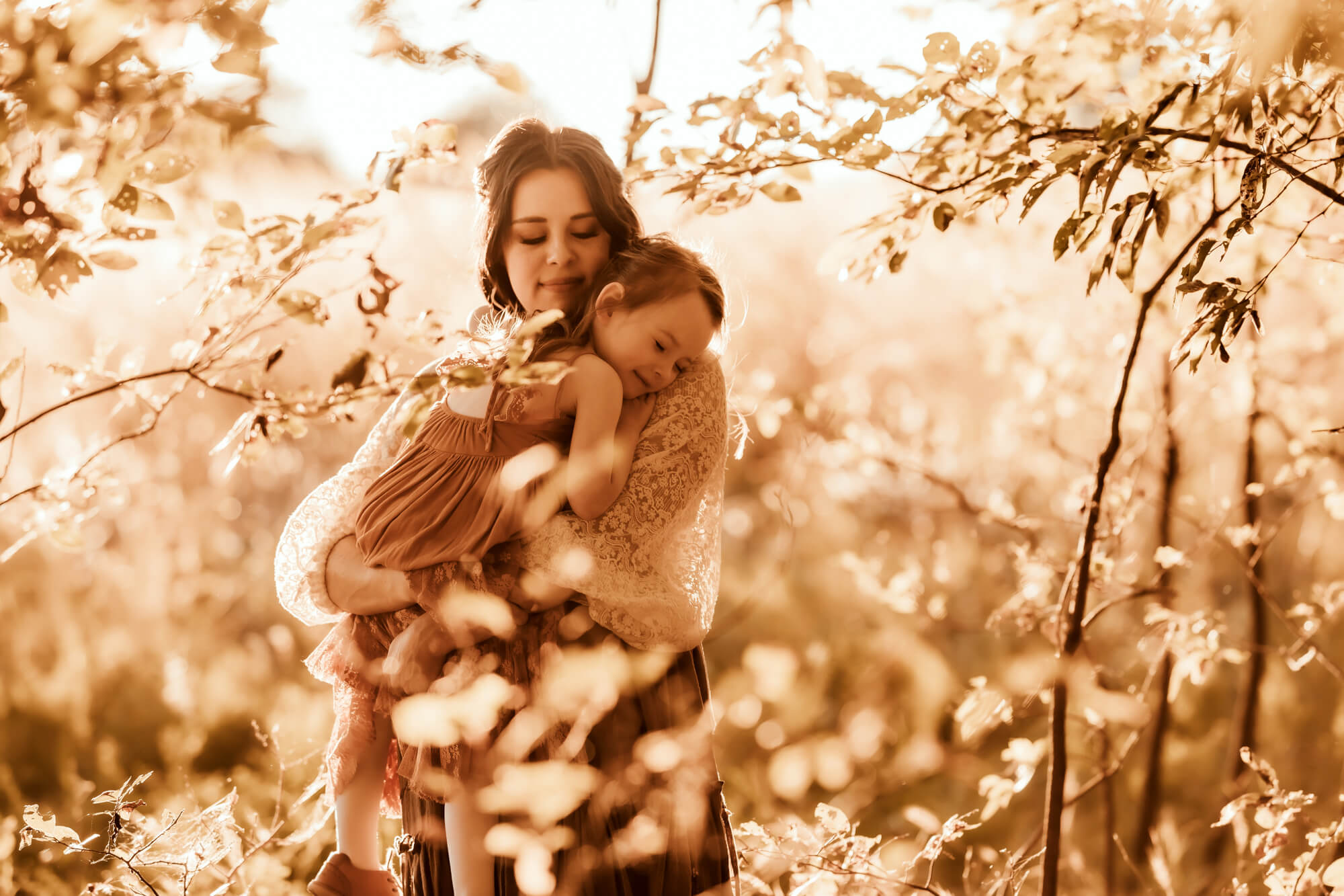 Mother holds her daughter with leaves surrounding them.