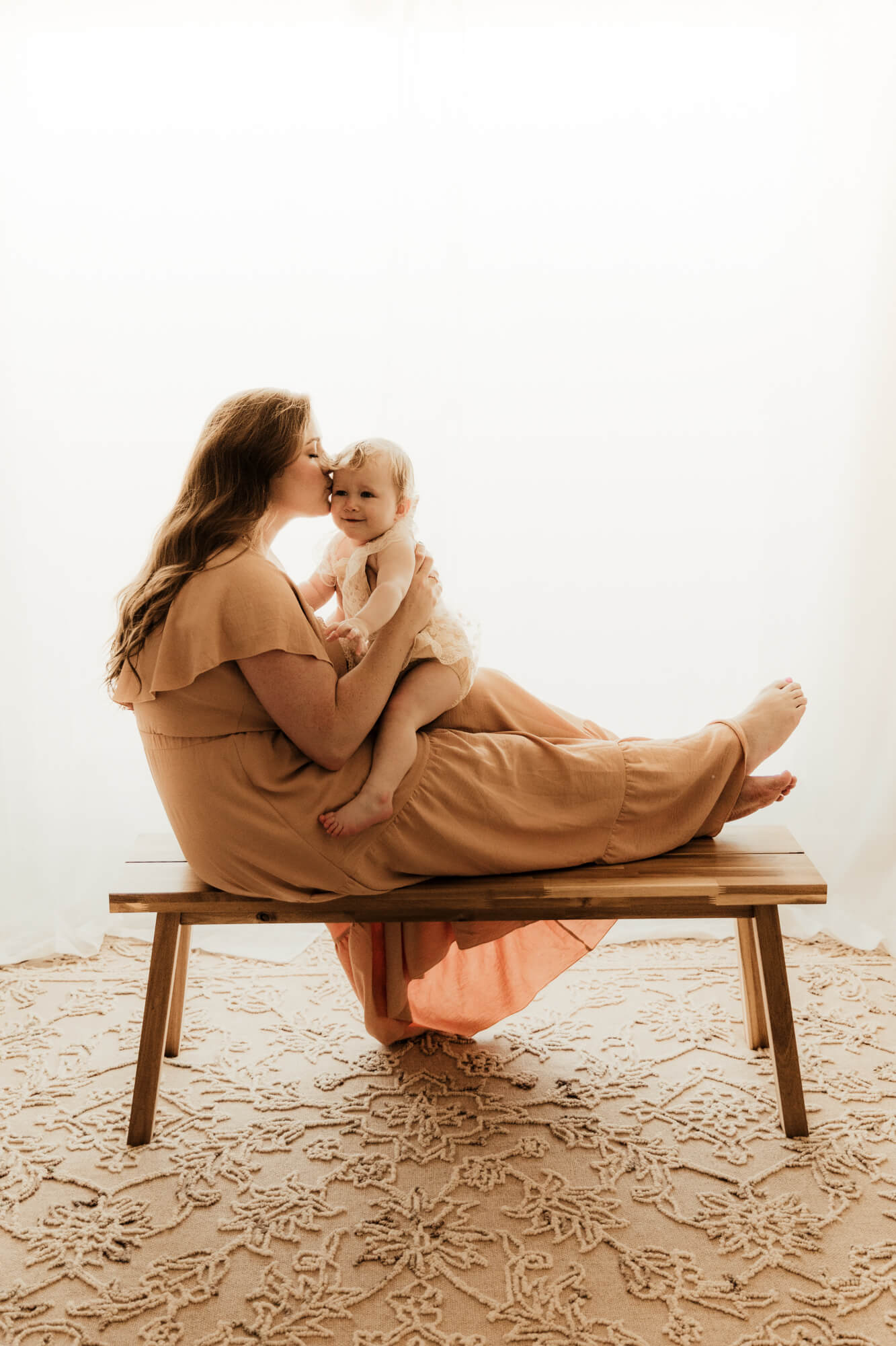 Mother kisses her daughter while sitting on a bench.