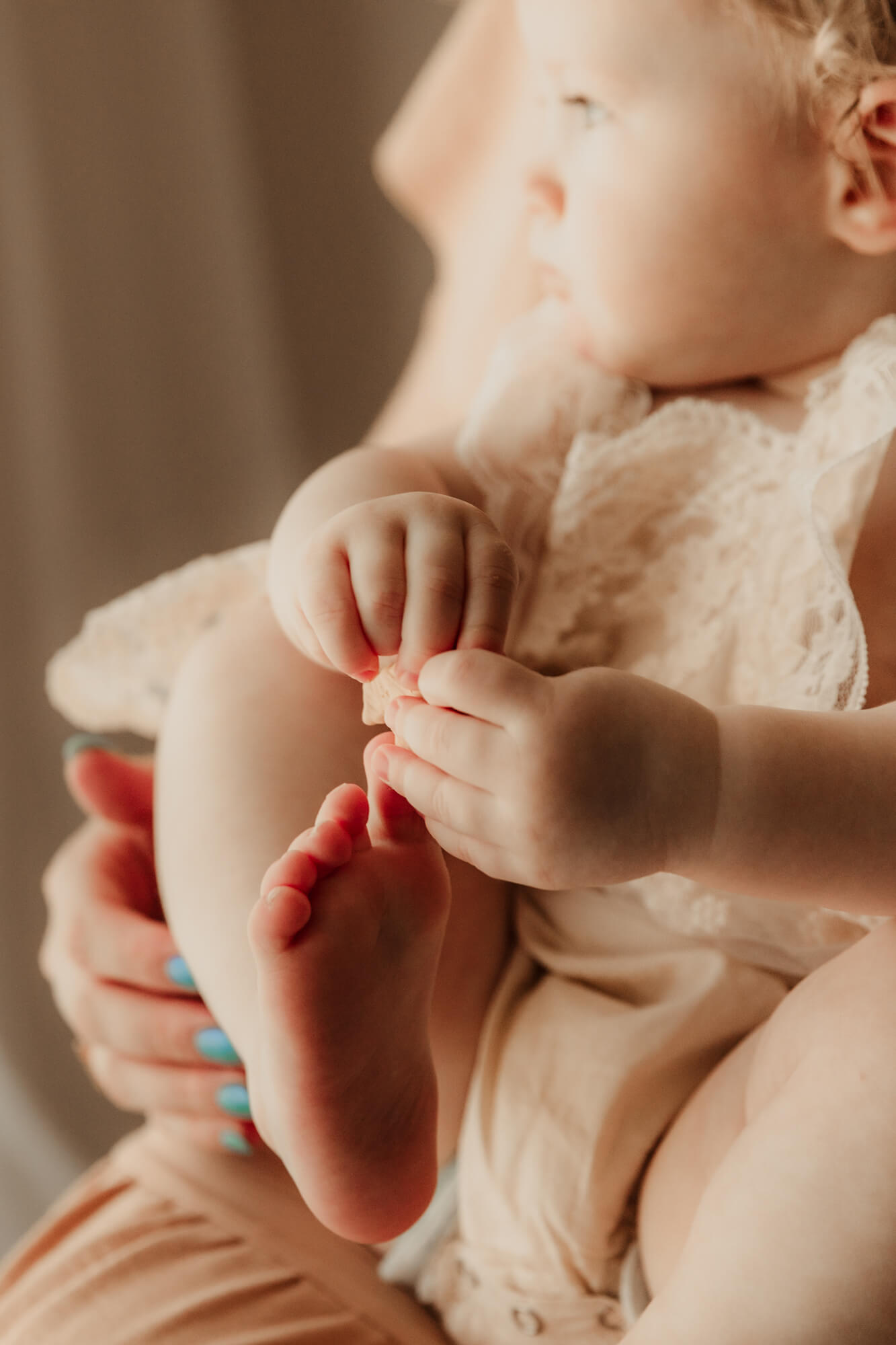 Baby girl plays with her toes for a milestone family session in an OKC studio.