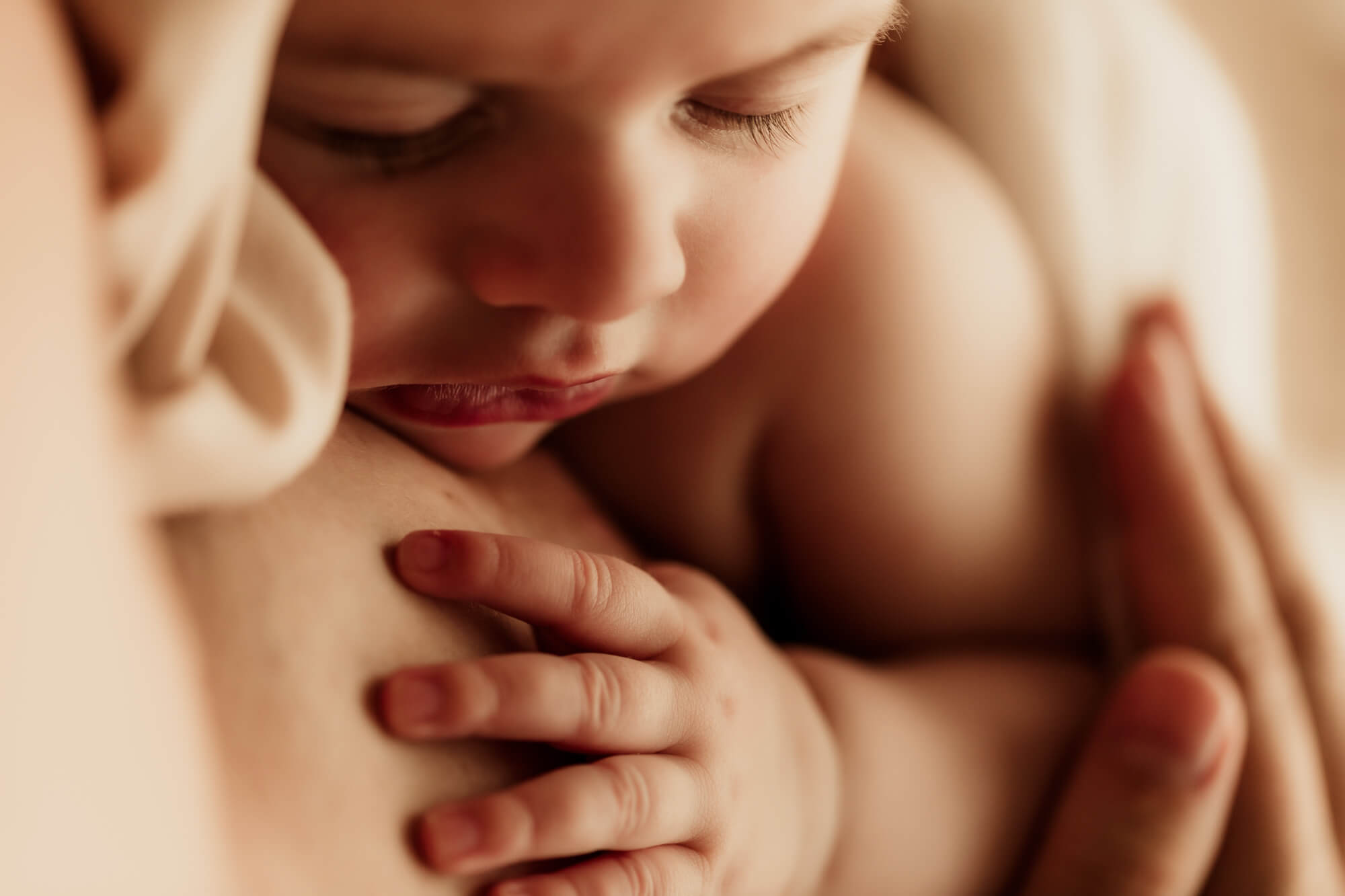 Baby girl sleeping on her mother with her hand near her face.