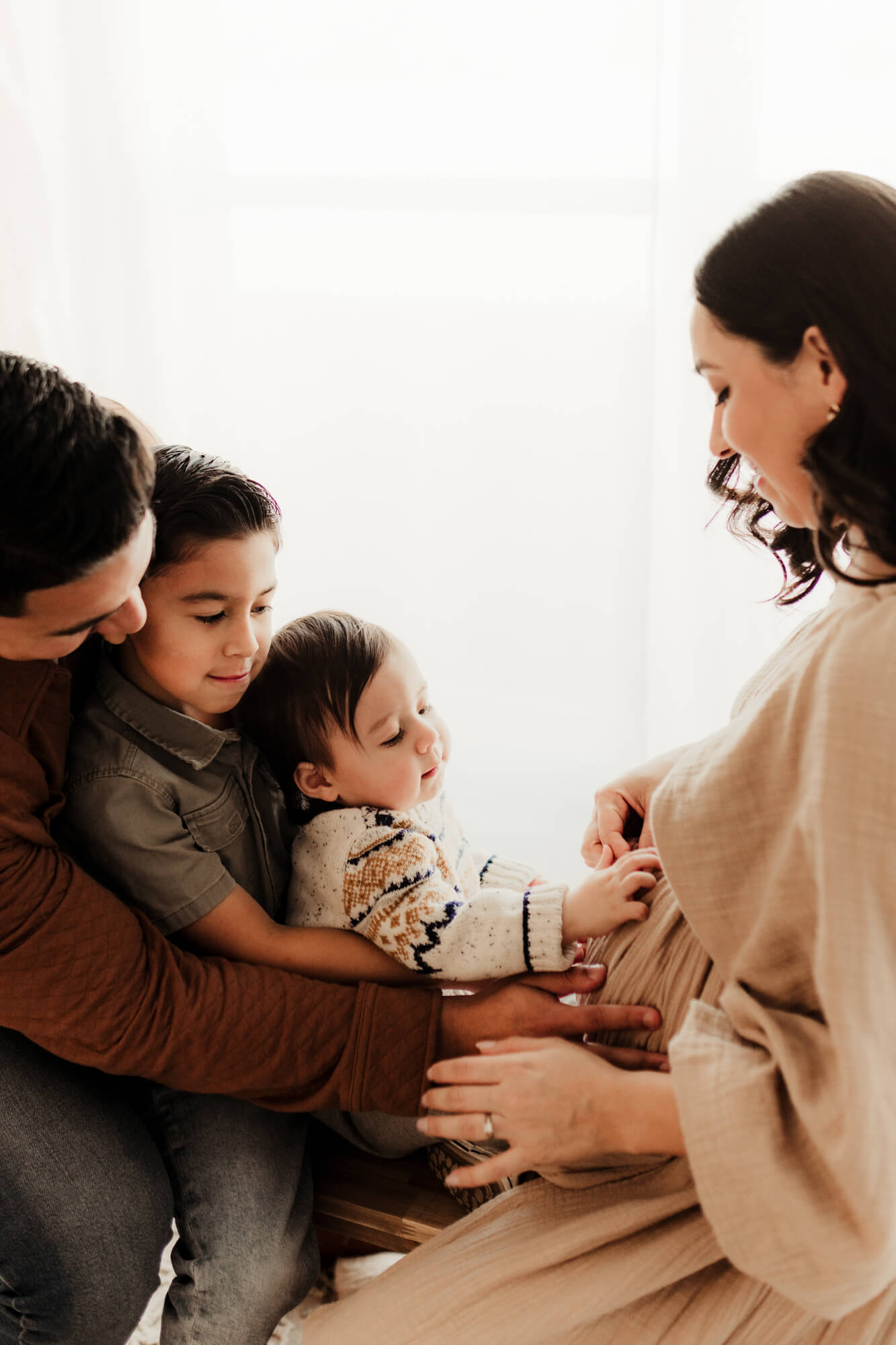 Husband and two sons touch the mother's pregnant belly.