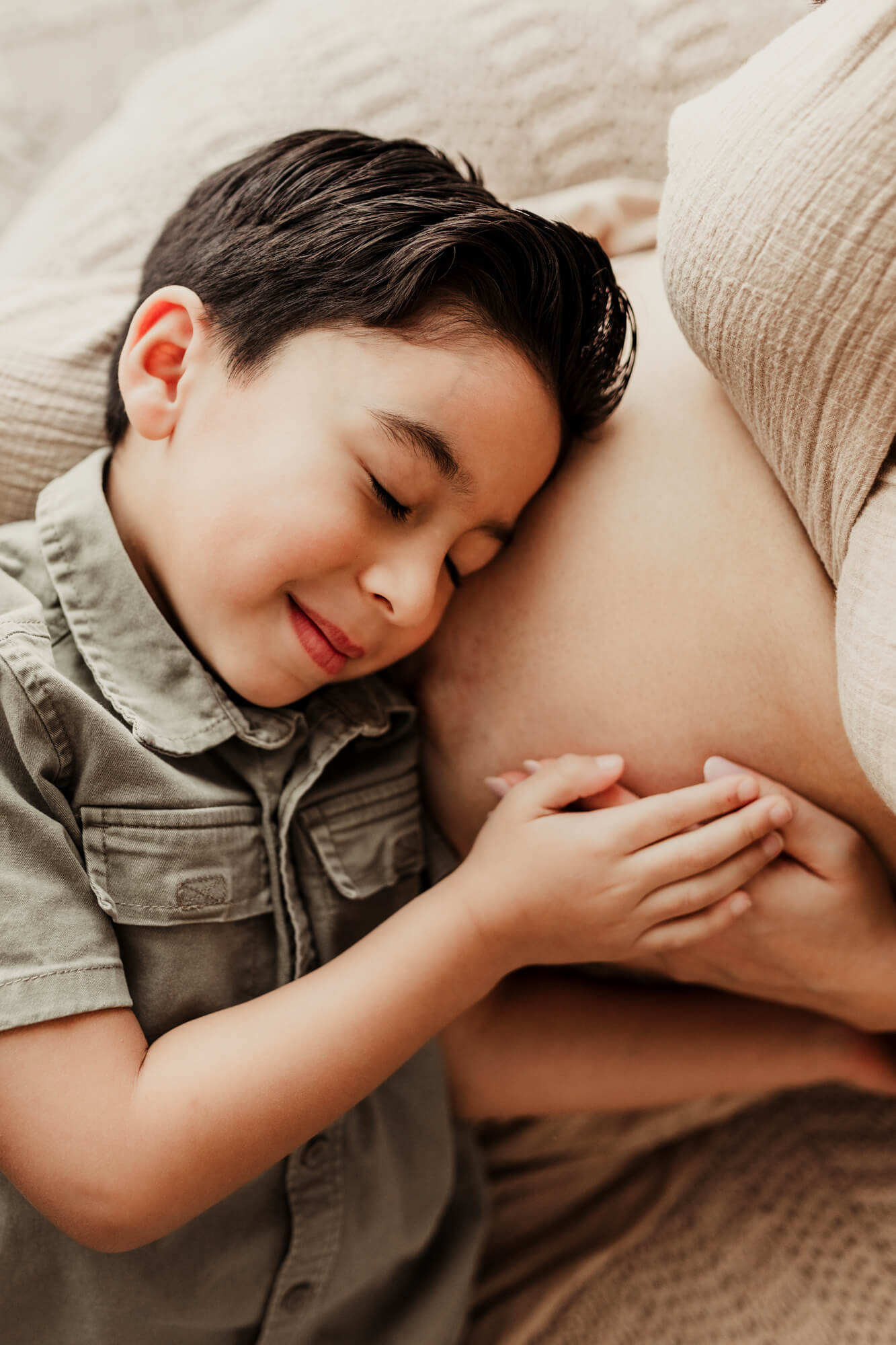 Son snuggles his mother's belly while laying down.