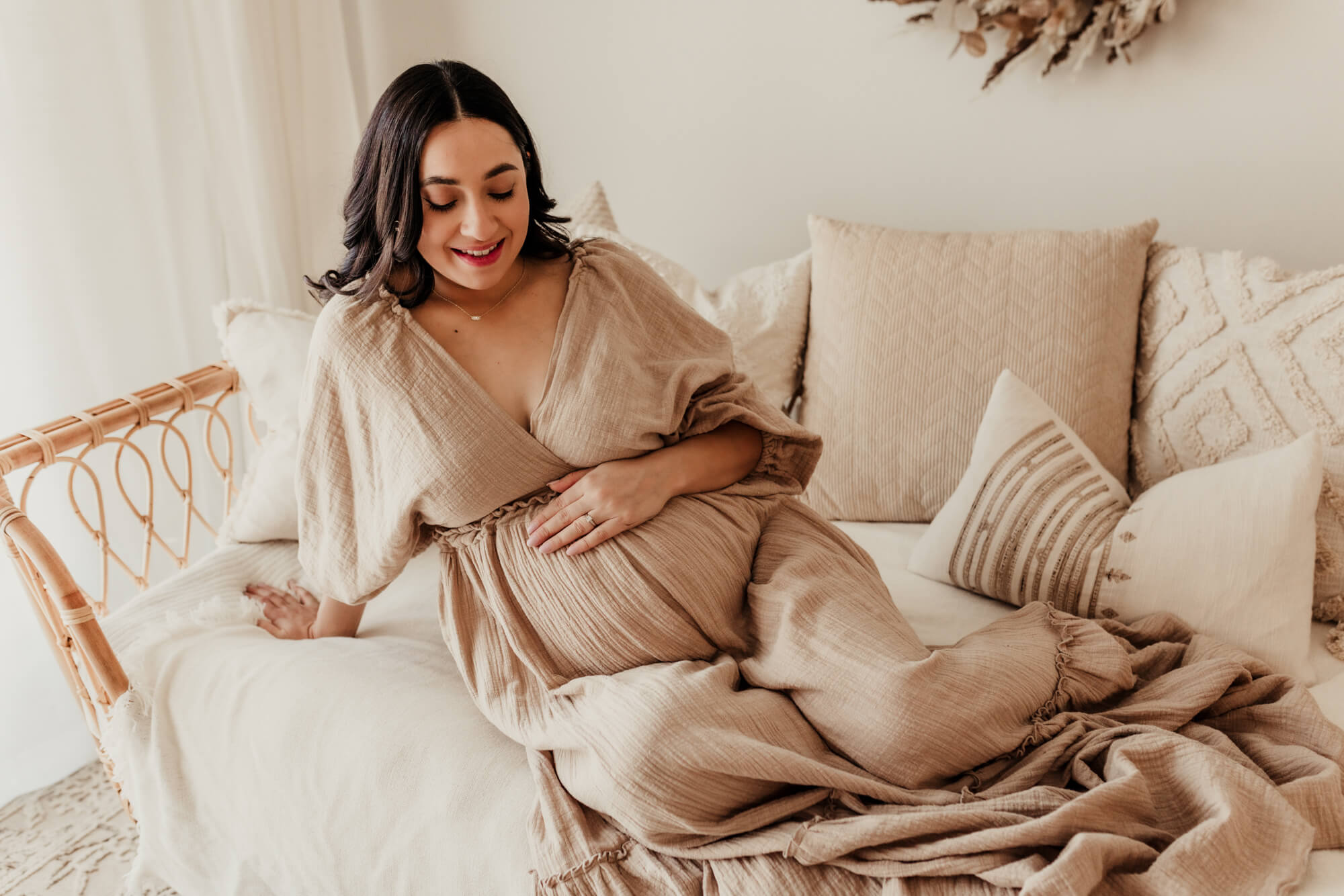 Pregnant woman sits on a rattan daybed with her hand on her belly, birthing center okc.