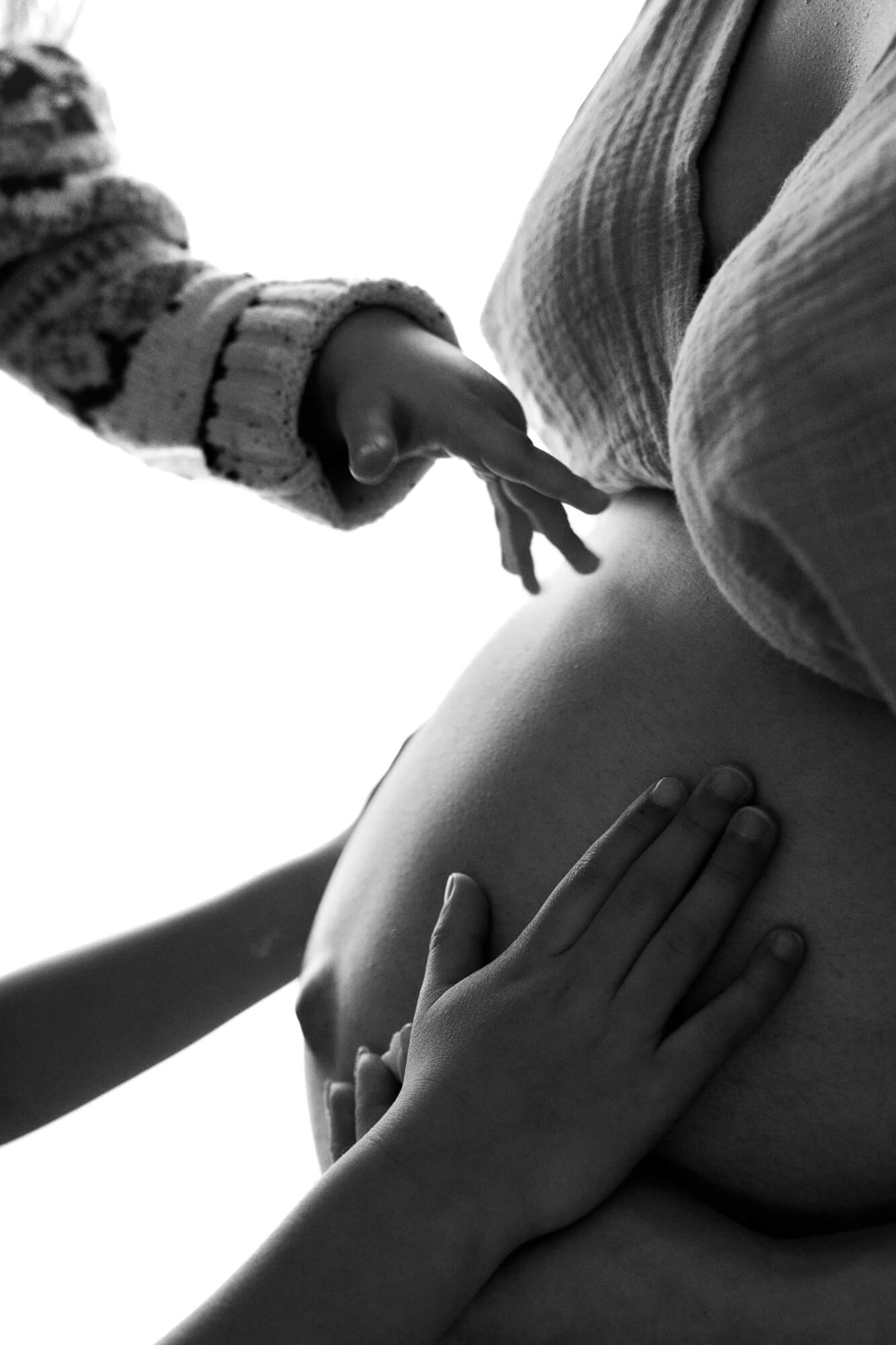 Black and white photo of two boys placing their hands on their mother's pregnant belly,