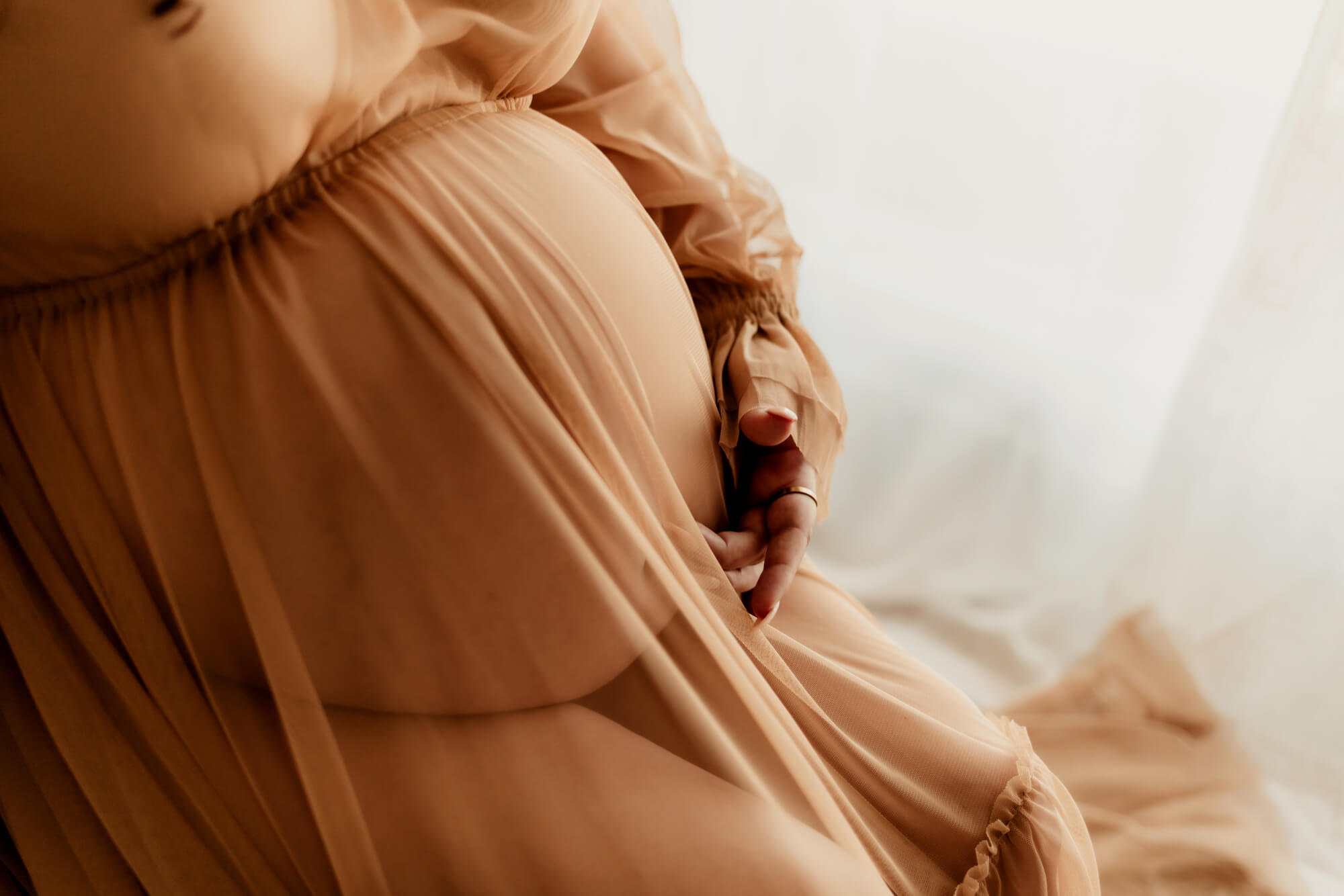 Details of a mom to be's bump in a sheer dress with a hand on her bump thanks to a Tulsa Fertility Center