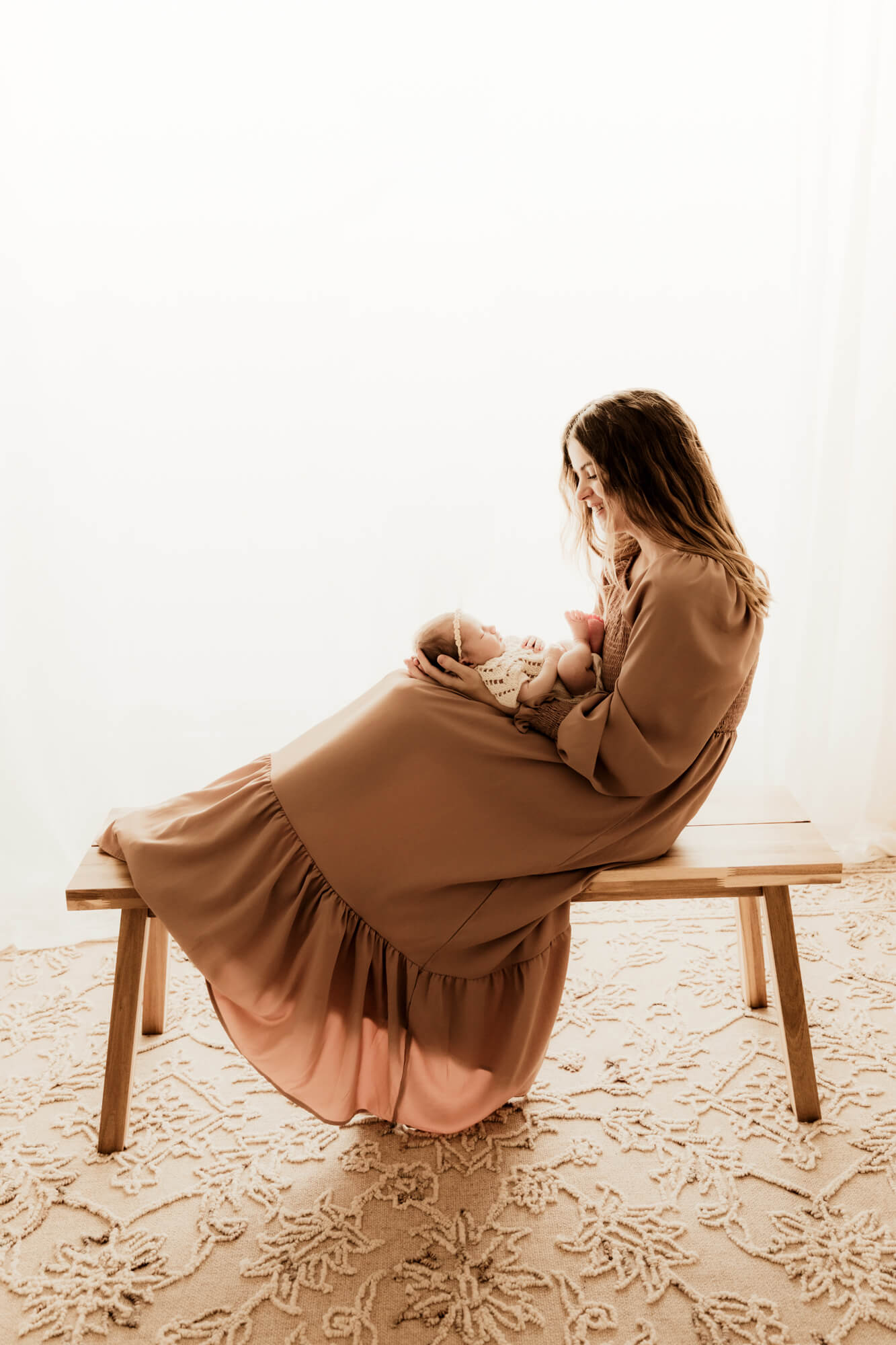 A happy mom sits across a wooden bench with her newborn baby sleeping in her lap thanks to Fertility Clinics in OKC