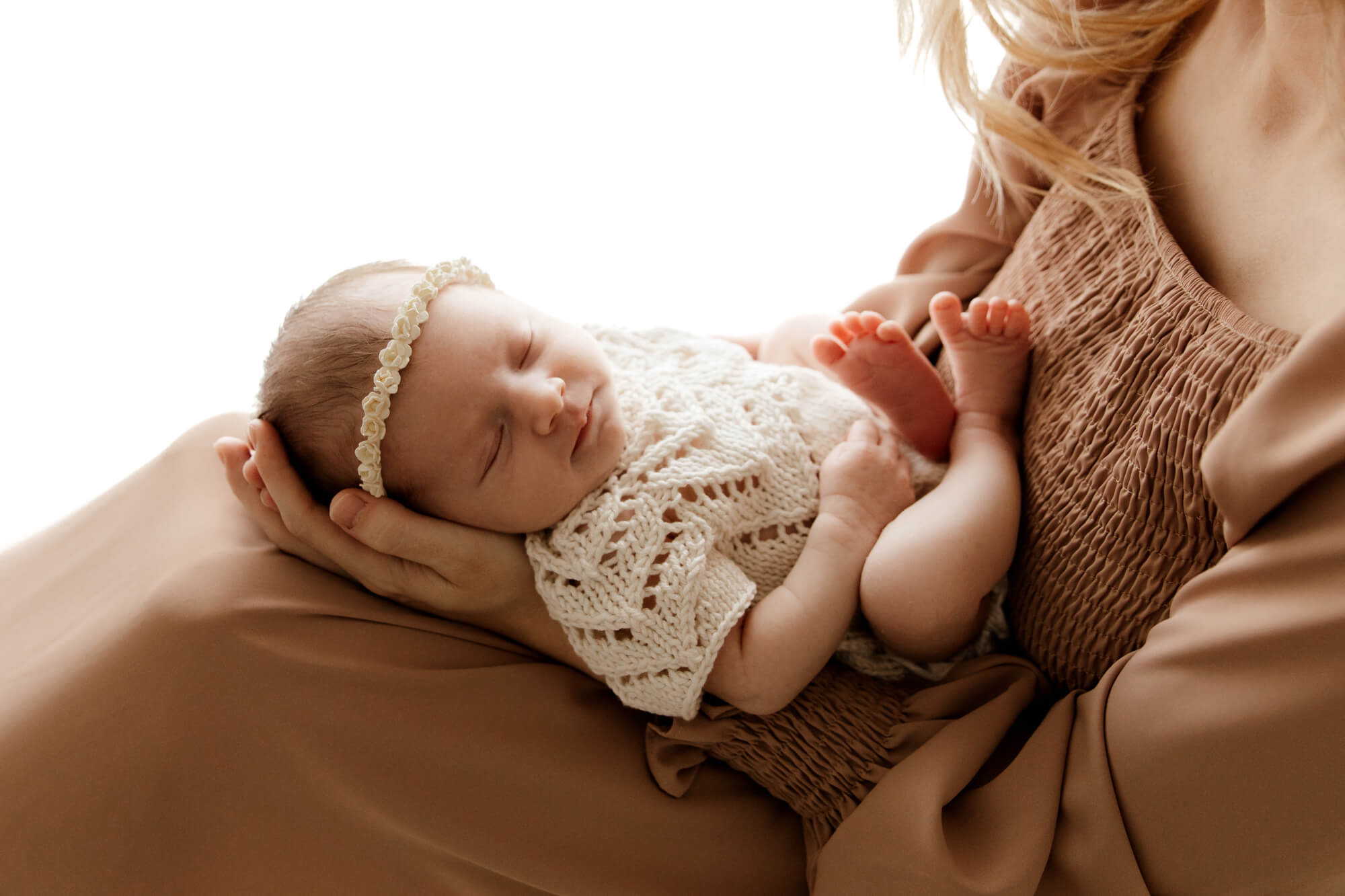 A newborn baby in a knit onesie sleeps in mom's lap thanks to Fertility Clinics in OKC