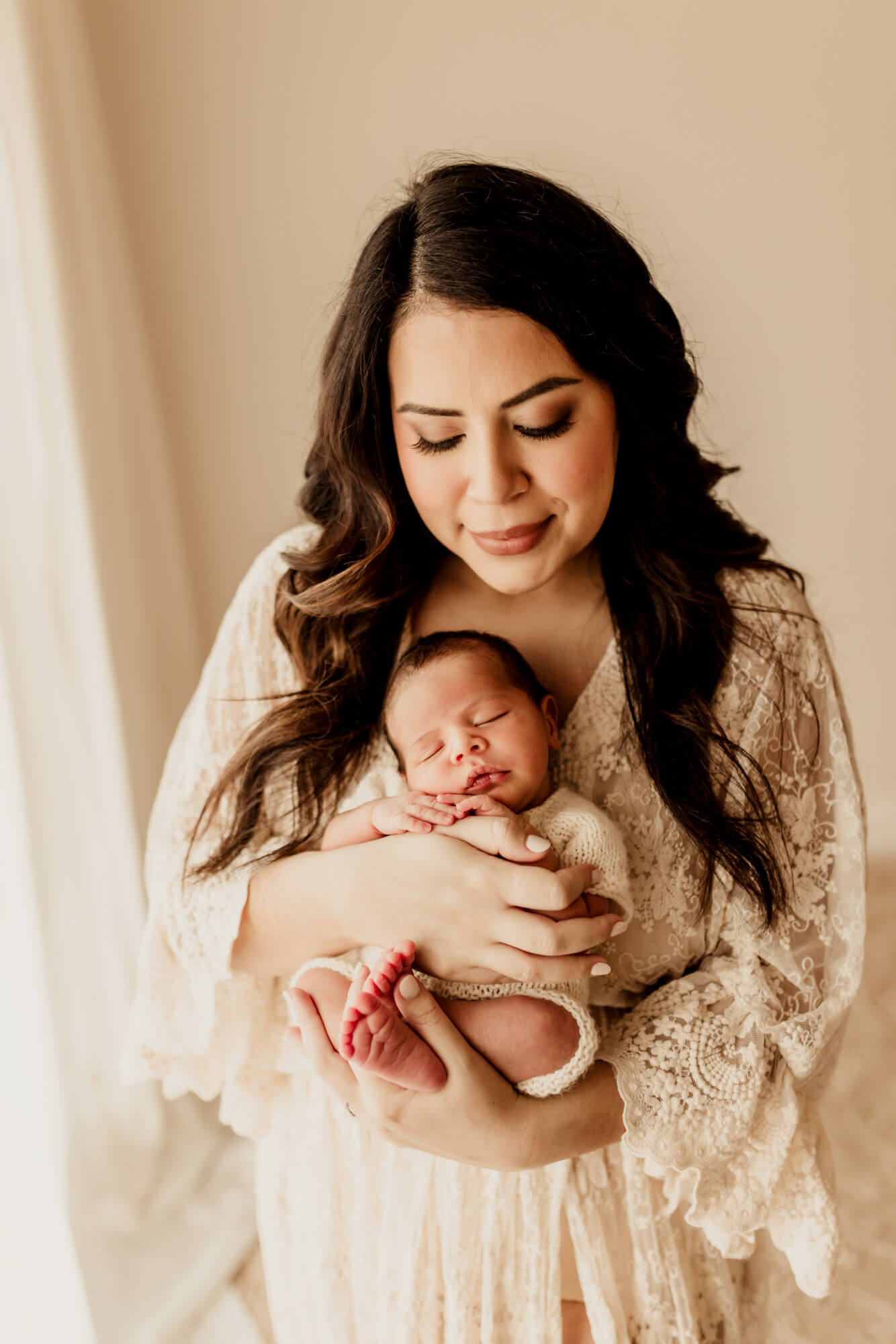 A sleeping newborn baby cradled against mom's chest as she stands in a lace gown