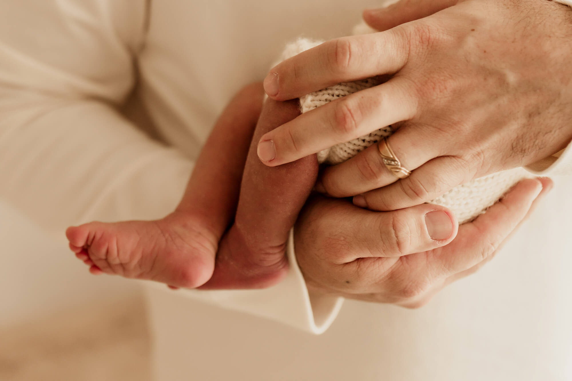 Details of a dad's hands holding his newborn baby before some swim lessons in Edmond, OK