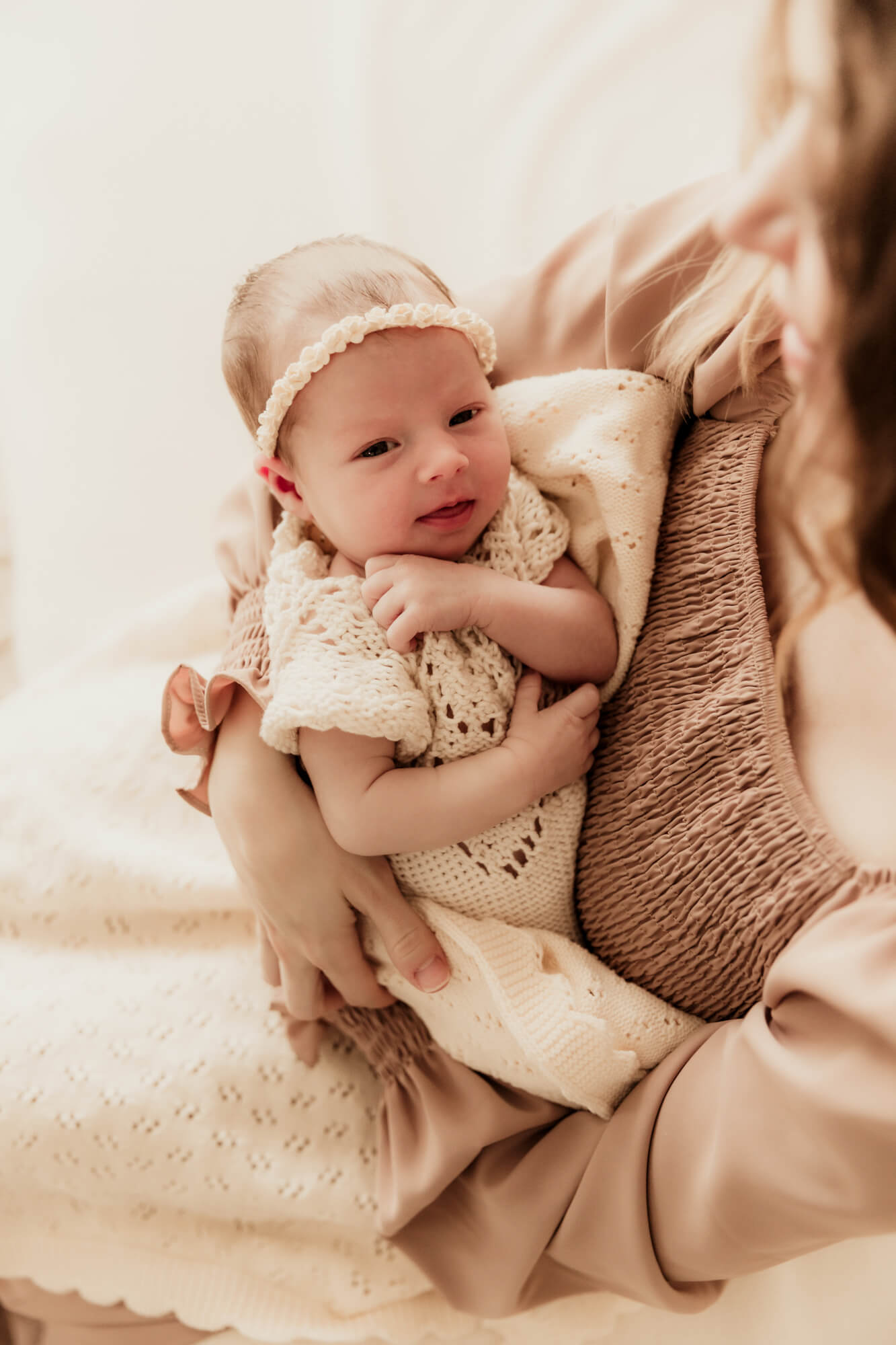 A newborn abby smiles while laying in mom's arms in a knit onesie after some OKC parenting classes