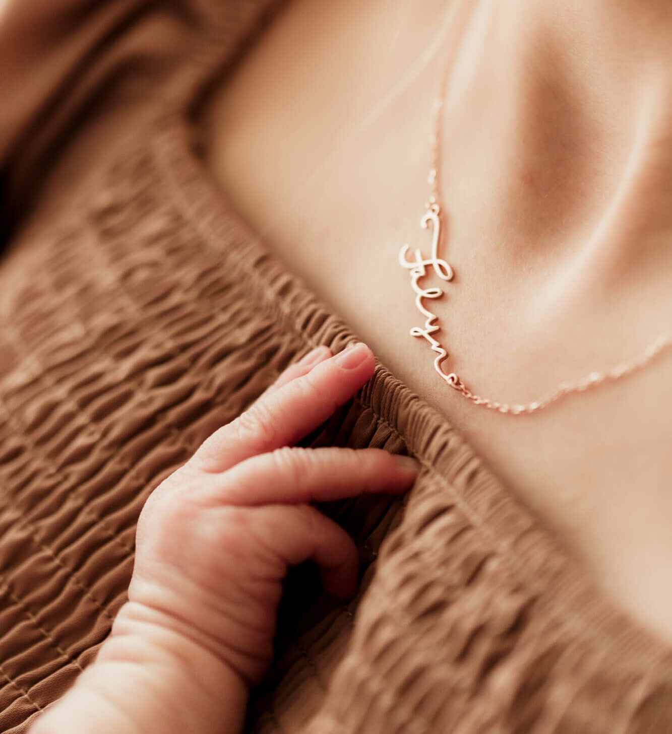 Details of a newborn baby's hand reaching for mom's necklace