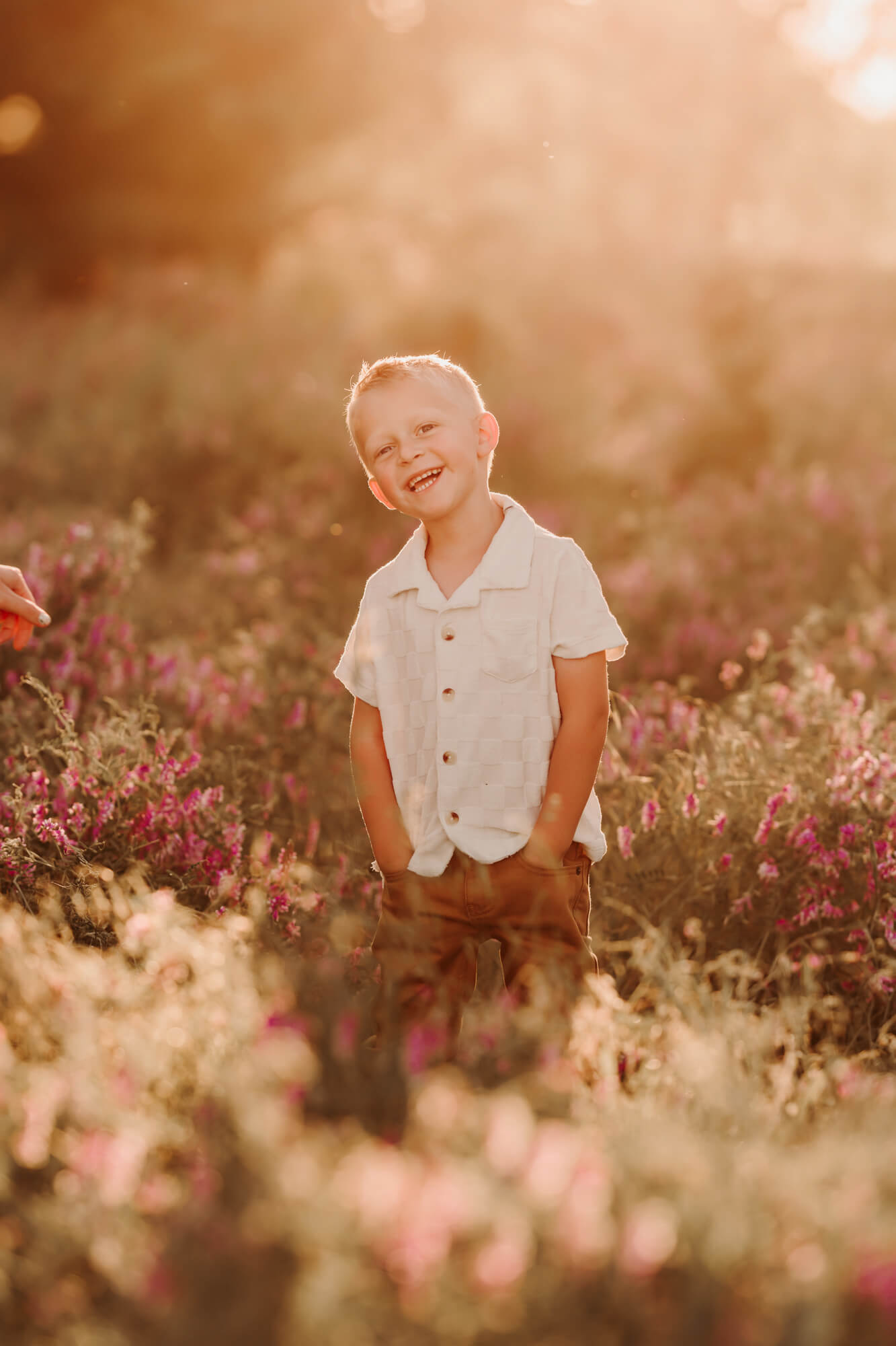 Boy with a white shirt and his khaki pants smiling with purple flowers surrounding him.