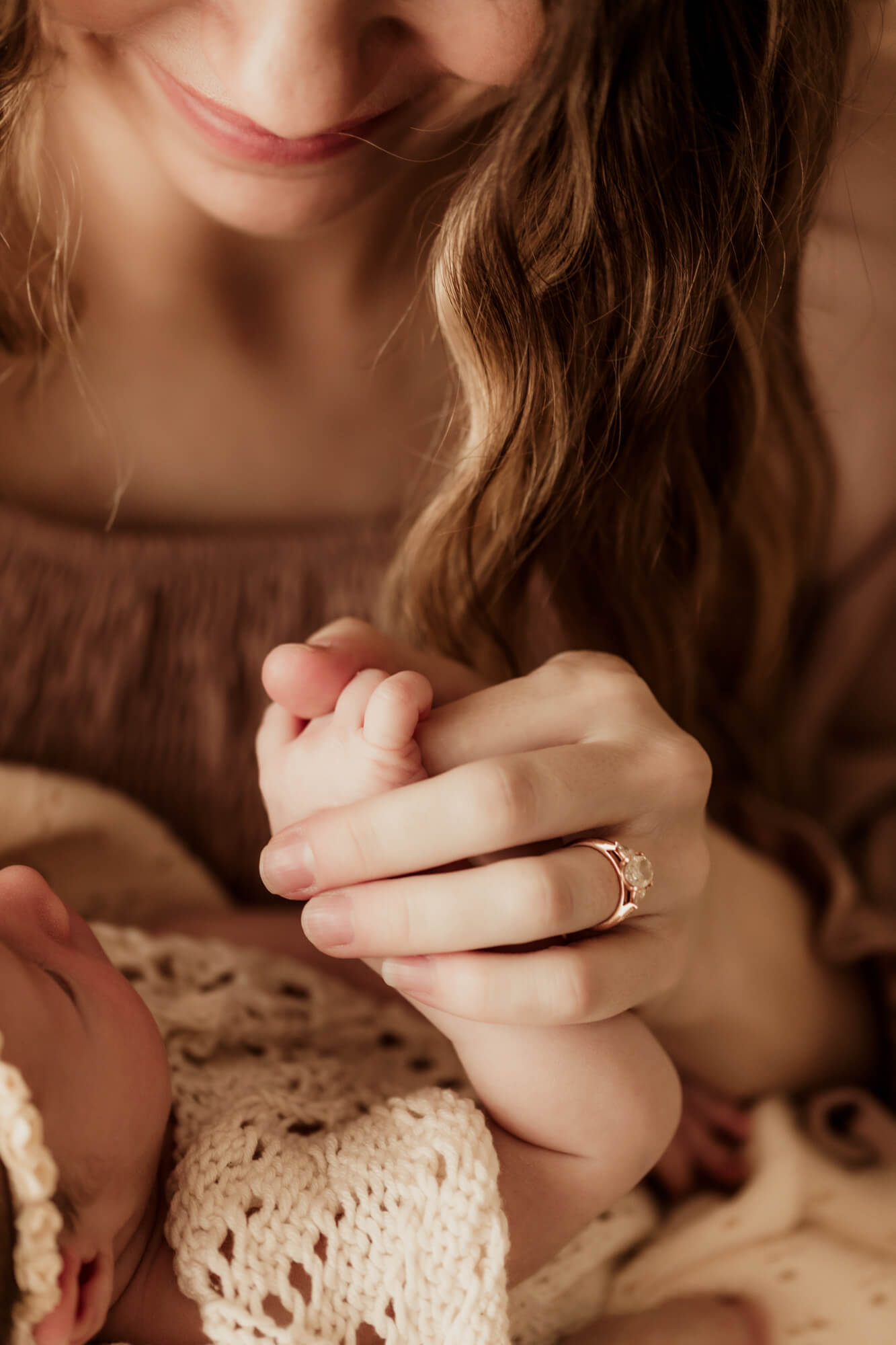 A newborn baby girl in a knit onesie holds mom's finger as she smiles down at her after visiting Tin Lizzies OKC