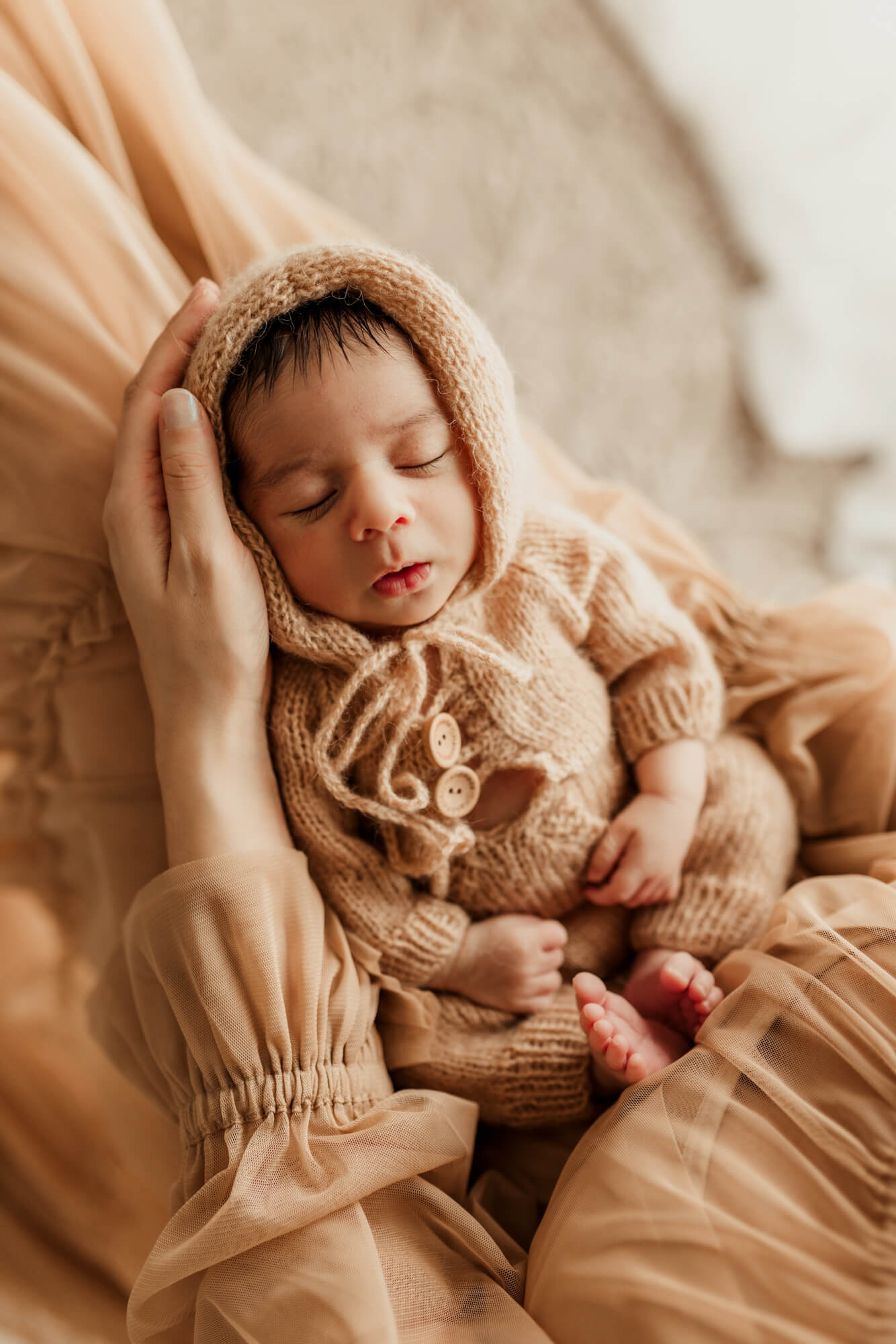 Baby boy wearing a tan knit romper sleeps while laying on his mother's lap, Perinatal Center of Oklahoma.