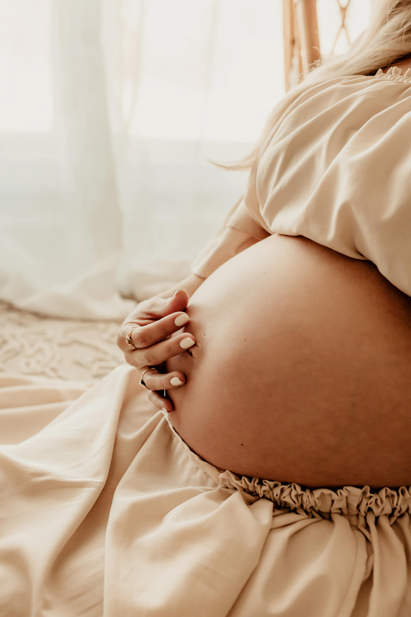 Details of a mom to be's hand on her bump in a beige two piece dress.