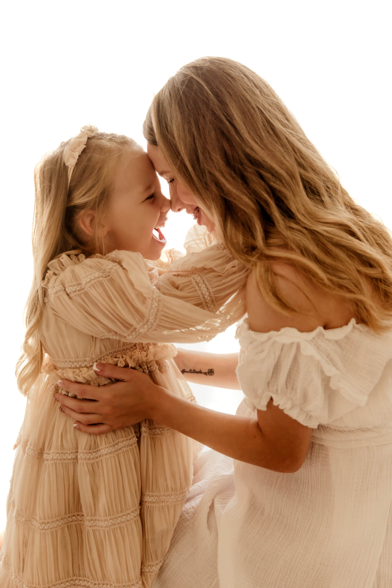 Mother and daughter smile at one another with their foreheads together.