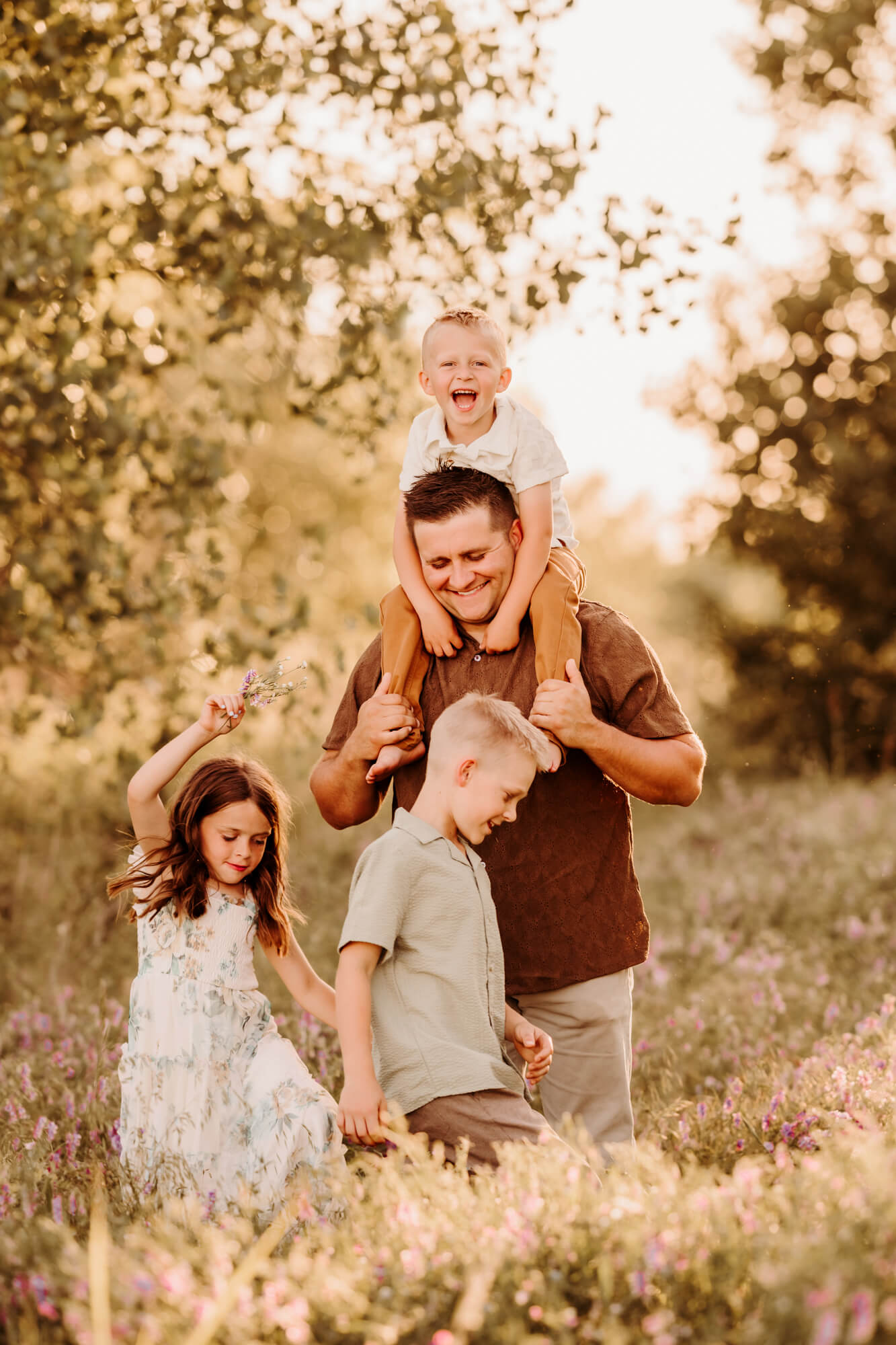 Father holds one son on his shoulders, while the other two children walk around.
