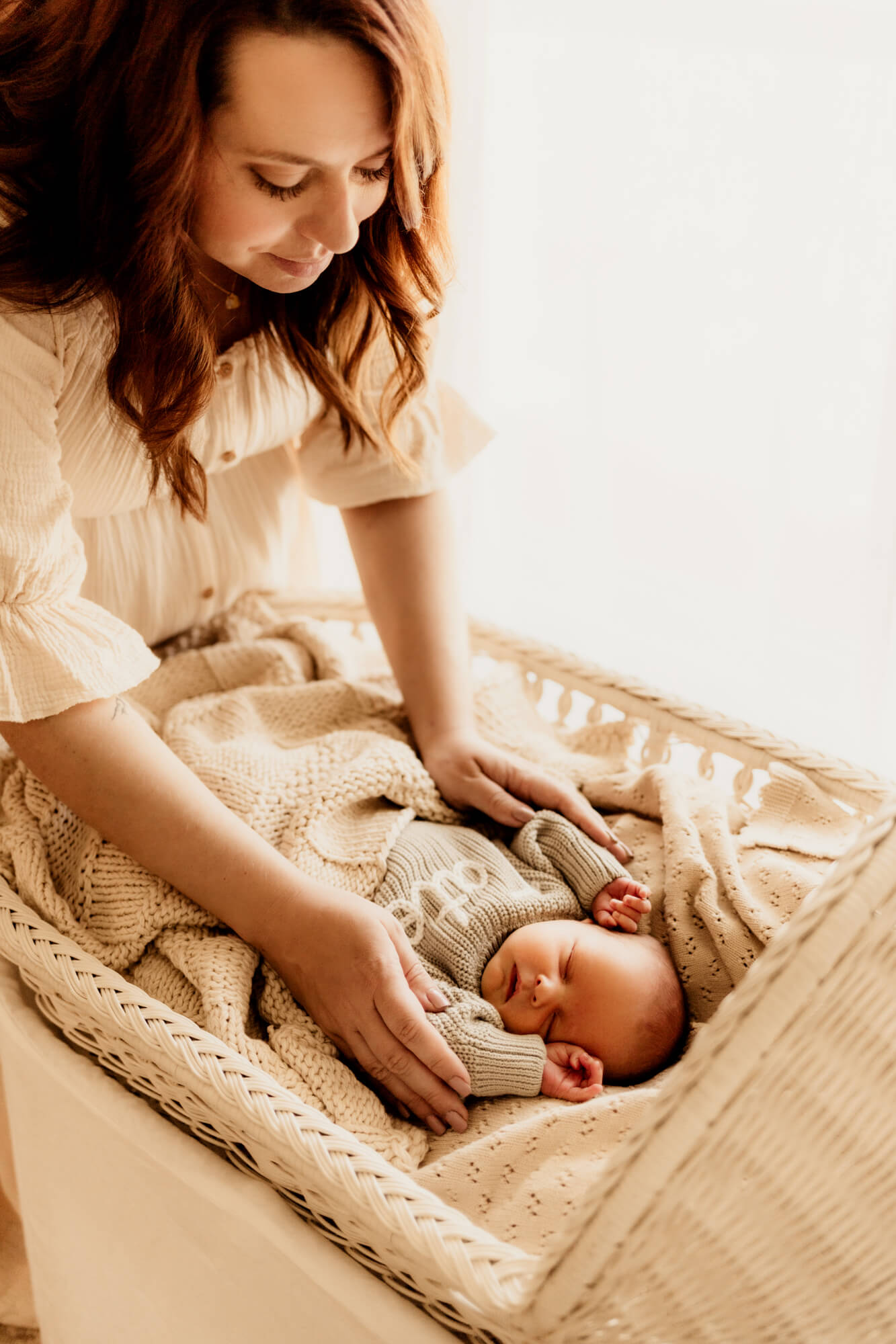 Mother wearing a cream colored dress looks at her baby boy in a white bassinet, Oklahoma City 3D ultrasound.