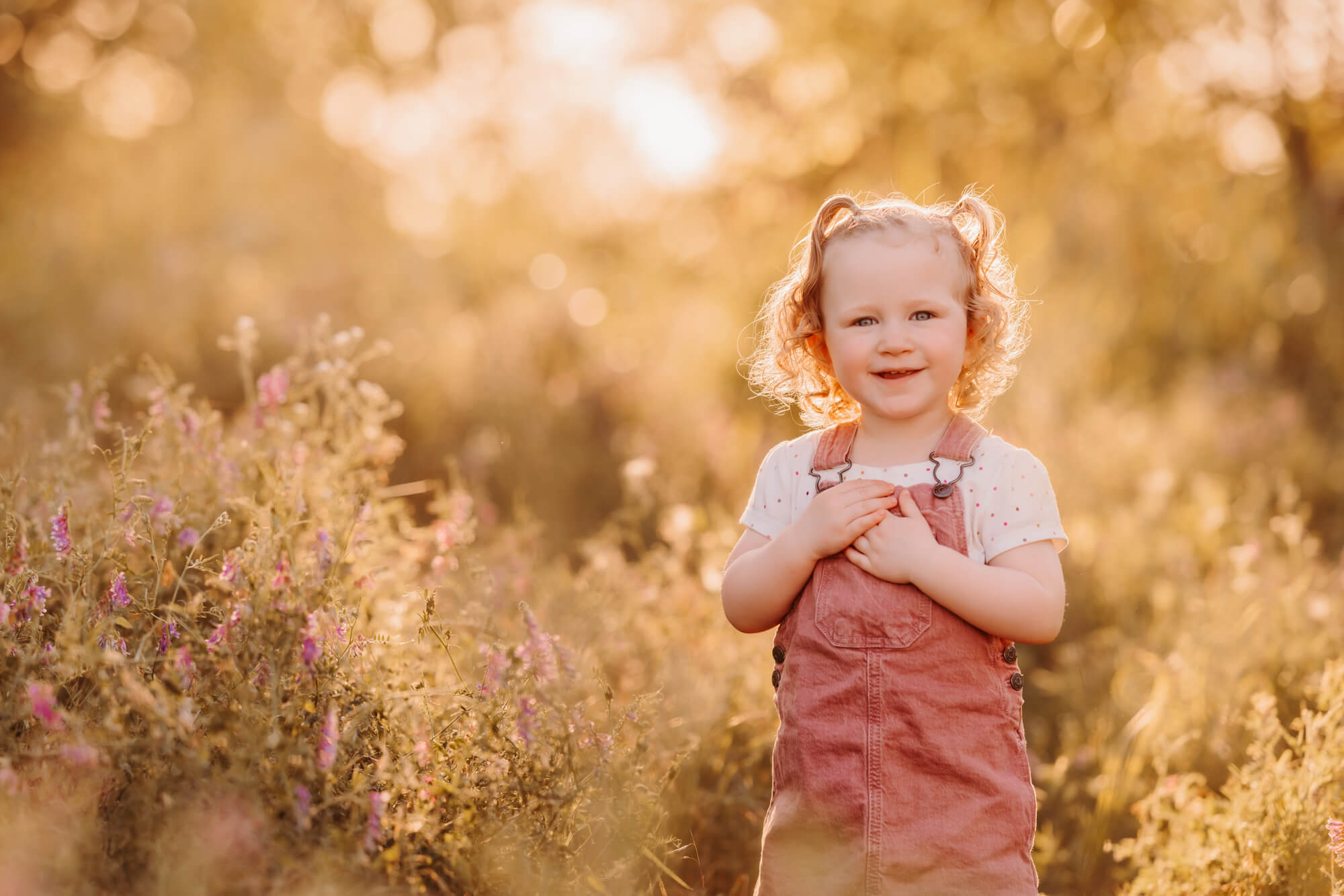 Girl wearing pink overalls places her hands over her heart and smiles in a field, kid friendly restaurants in OKC.