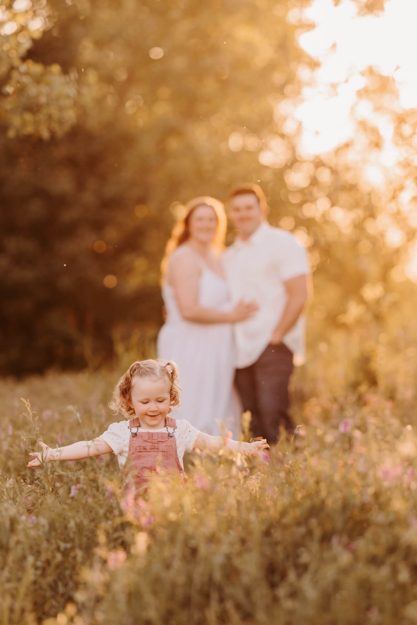 Girl plays in a field with her parents smiling behind her, kid friendly restaurants in OKC.
