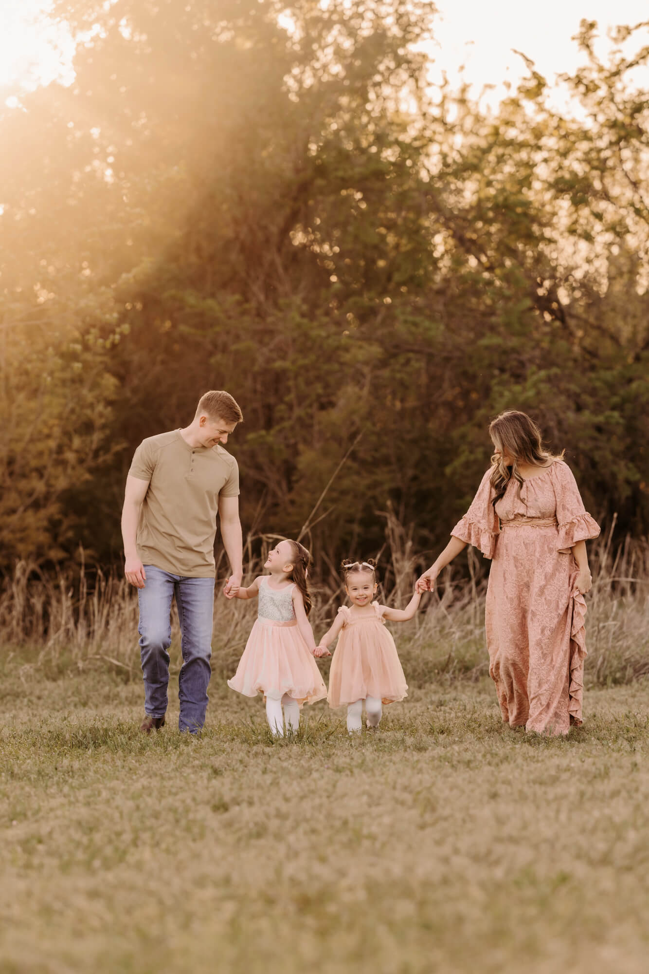 Family holding hands walk outside while smiling at one another.