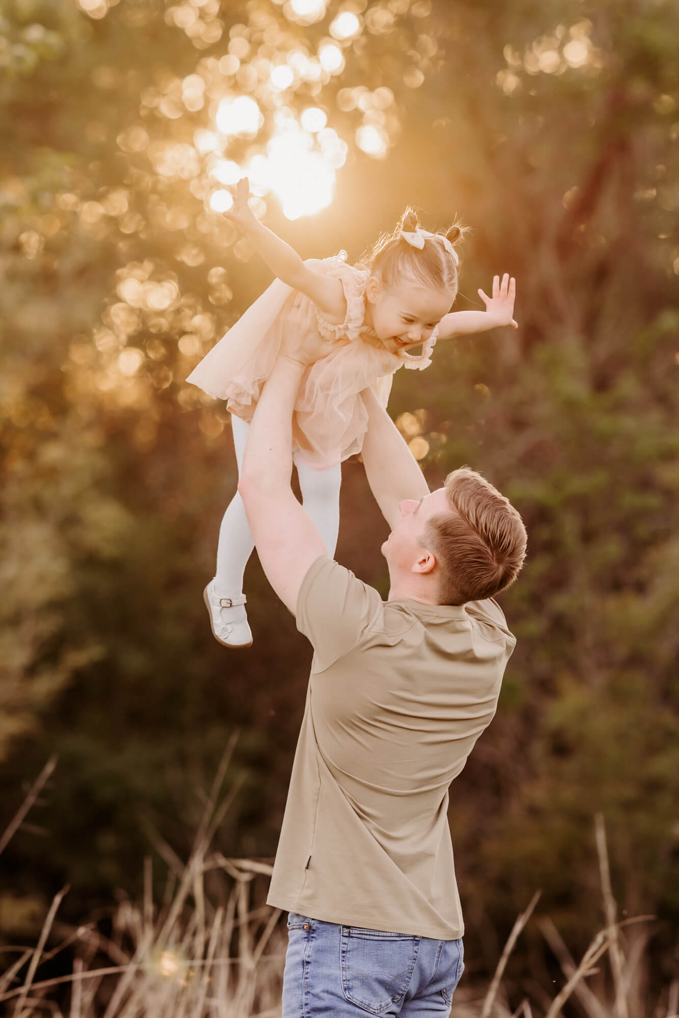Father holds his daughter  wearing a pink dress in the air during sunset, Montessori schools in OKC.