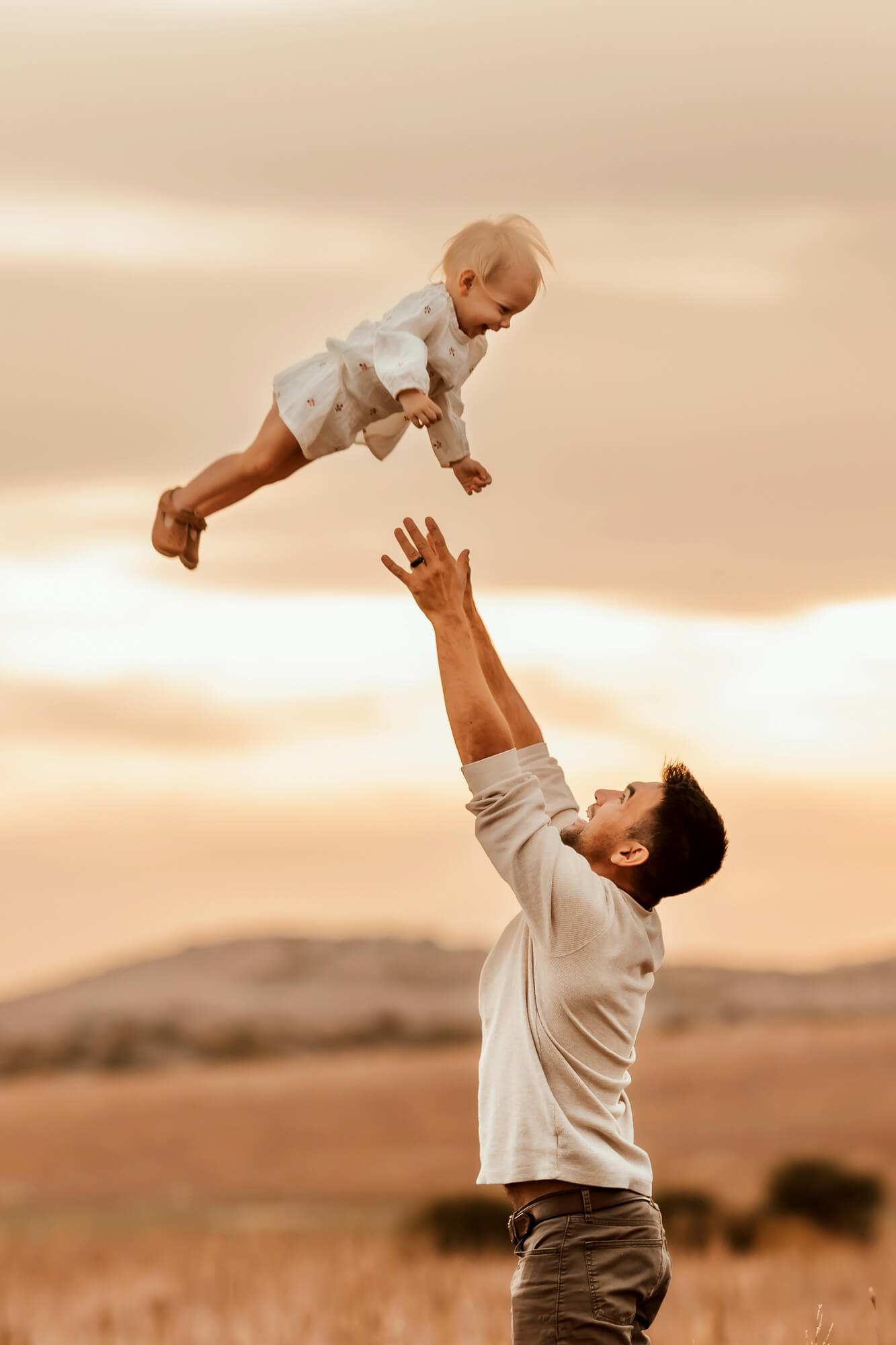 Father tosses his daughter in the air with the sun setting in the background, Kidoodles Norman OK.
