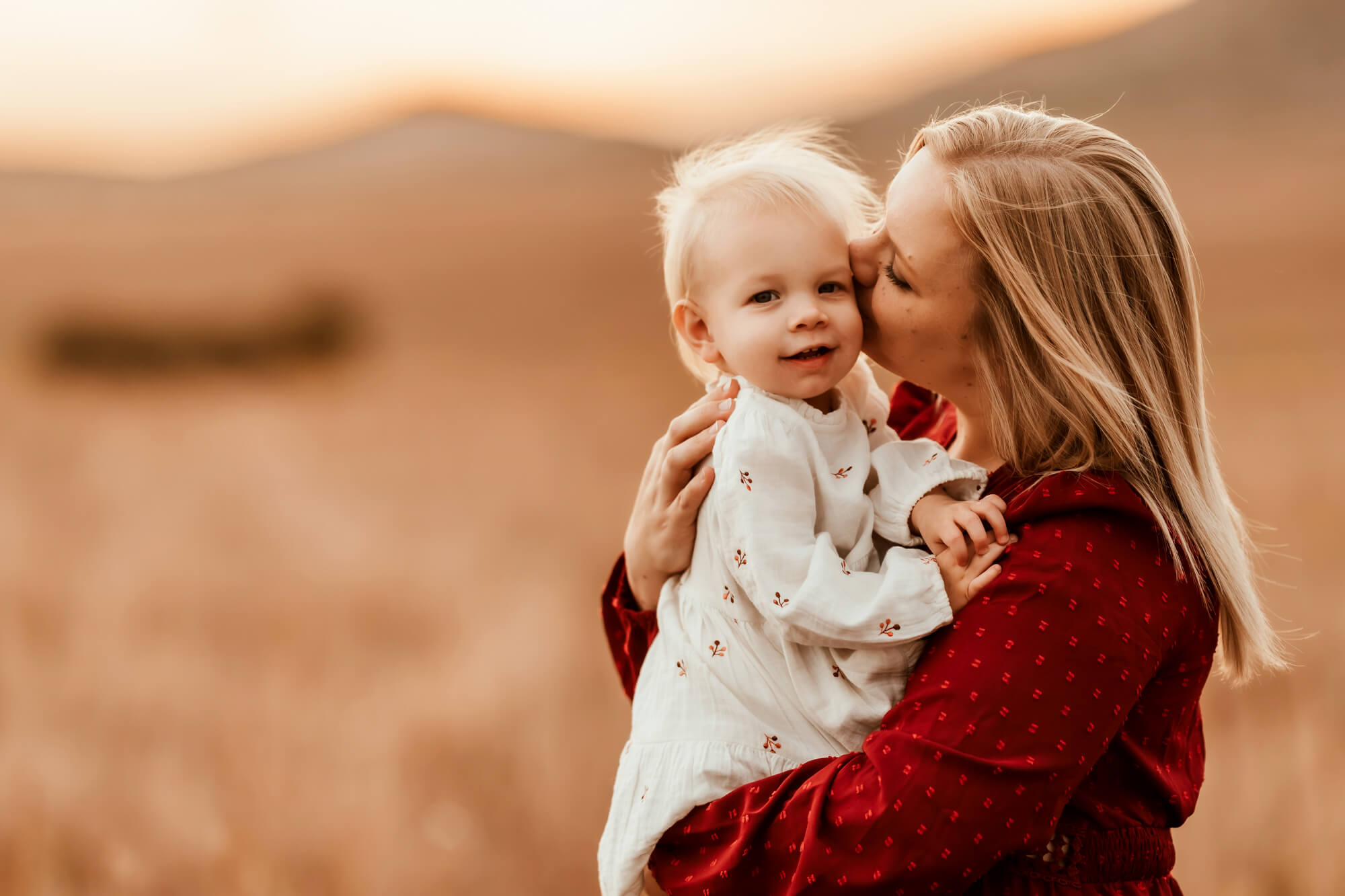 Mother with blonde hair and red dress kisses her daughter on the cheek, Kidoodles Norman OK.