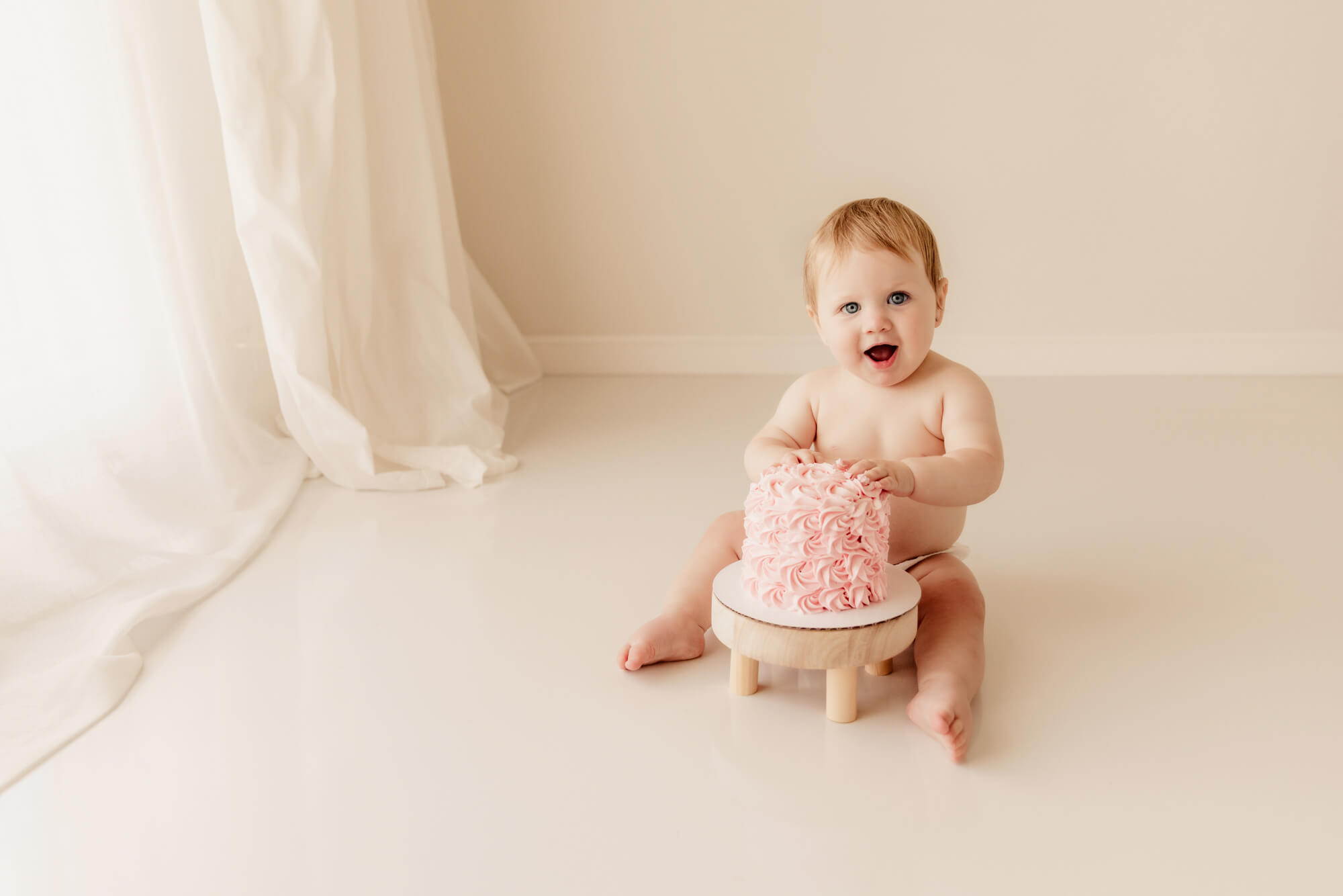 Baby girl sitting with on a white floor with her pink cake, OKC birthday party.