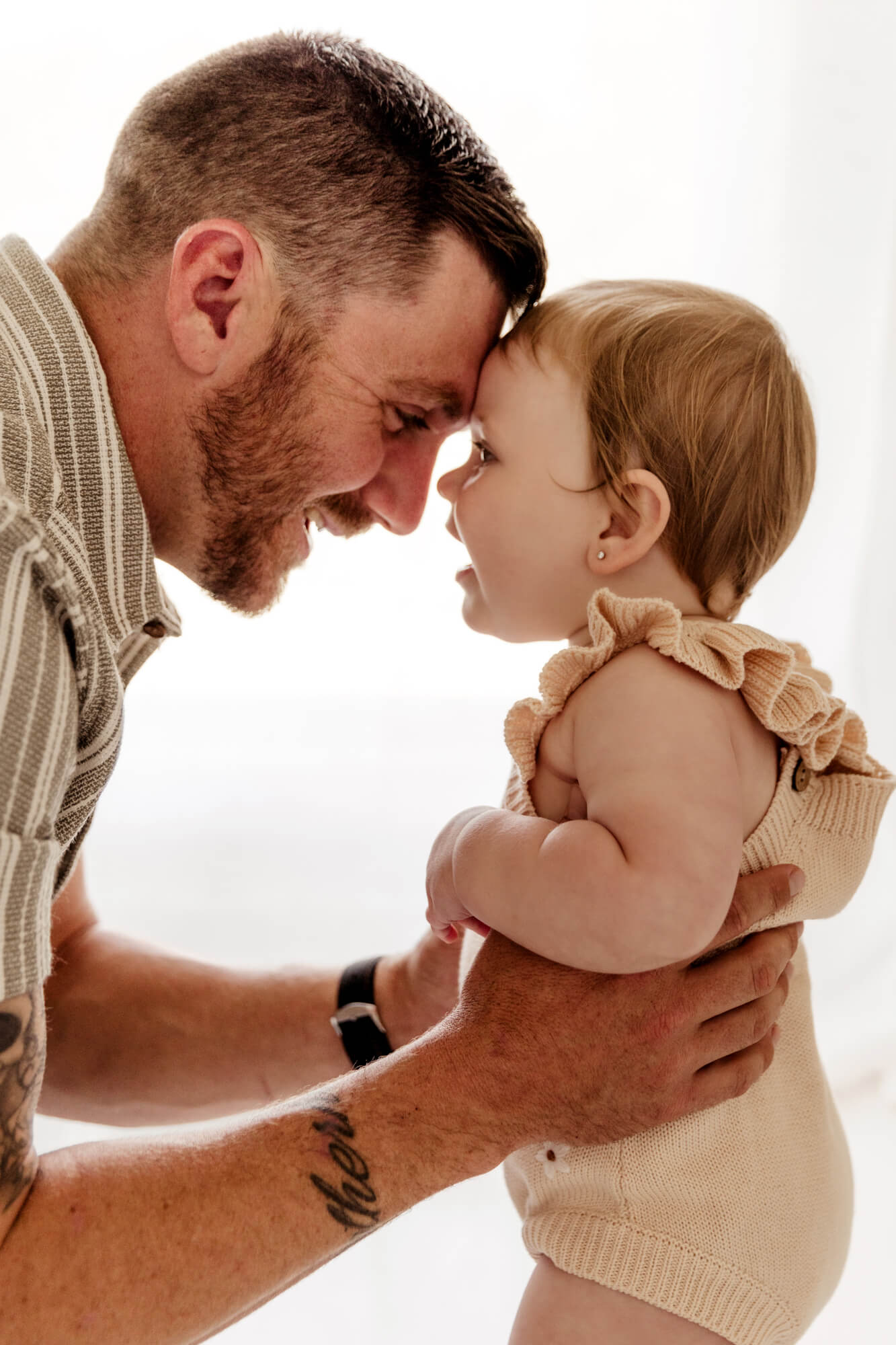 Father and baby girl touch foreheads while smiling at one another.