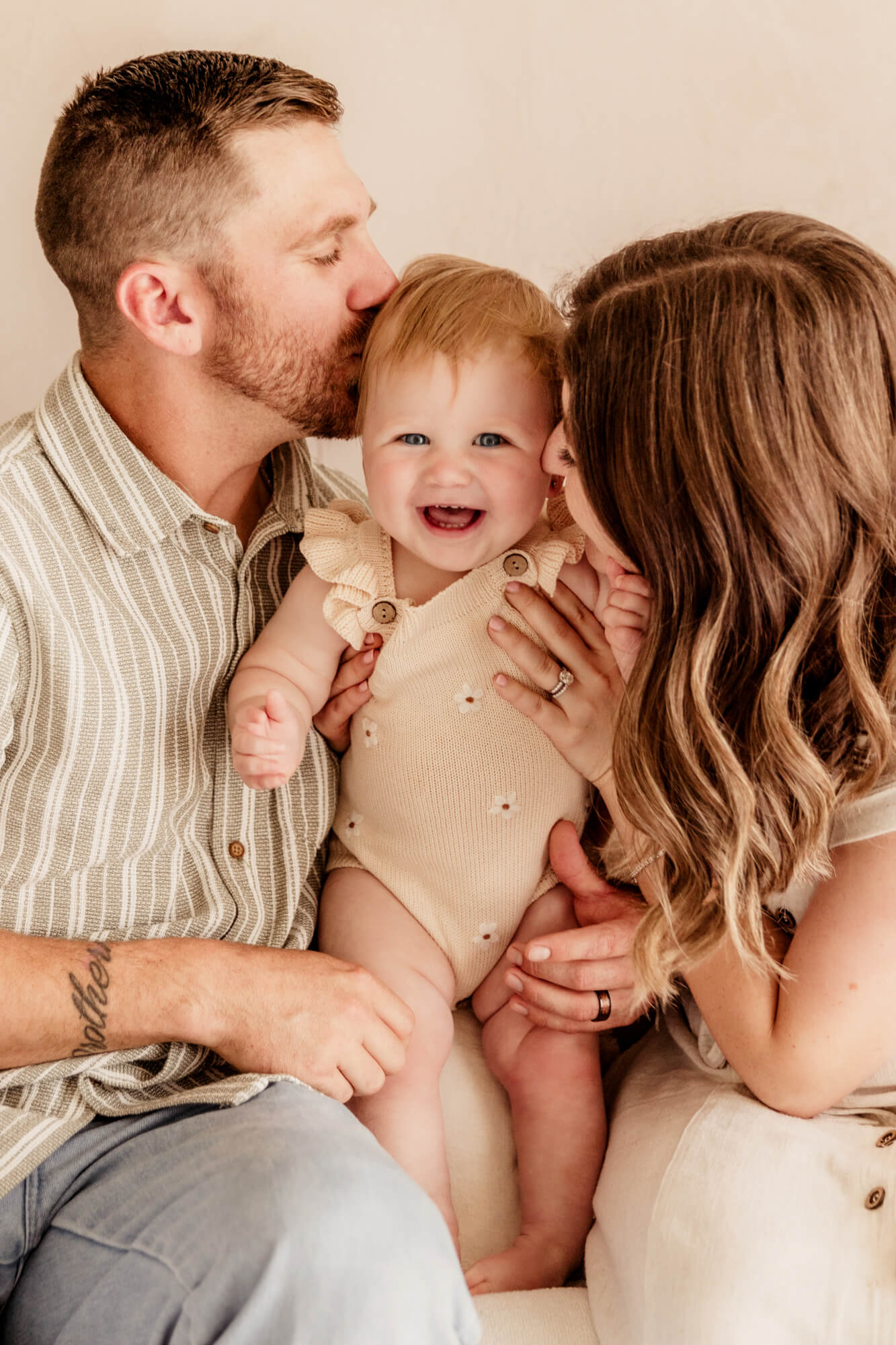 Mother and father kiss their baby girl on her face.