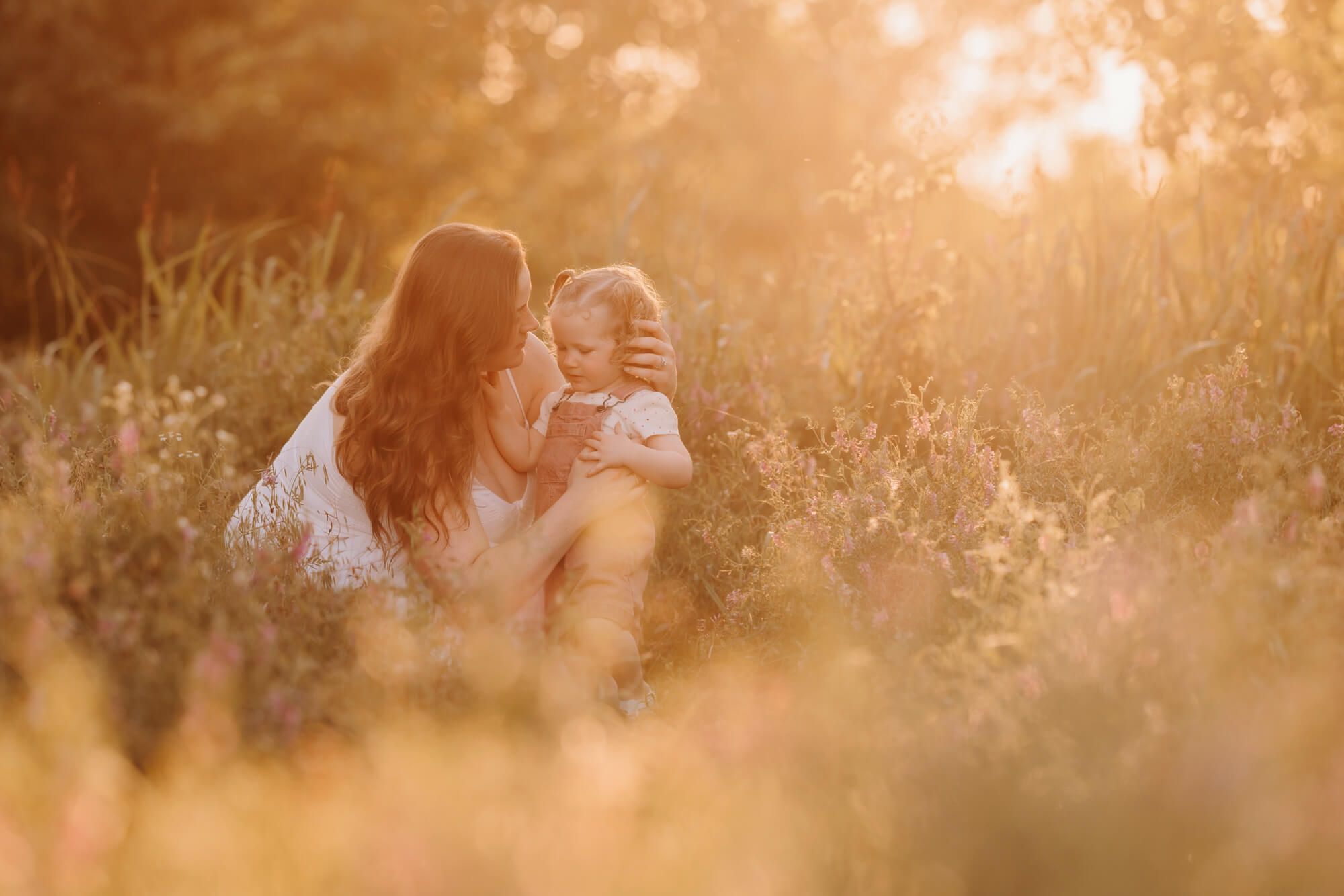 Mother stroking her daughter's hair while kneeling next to her in a field, OKC splash pads.