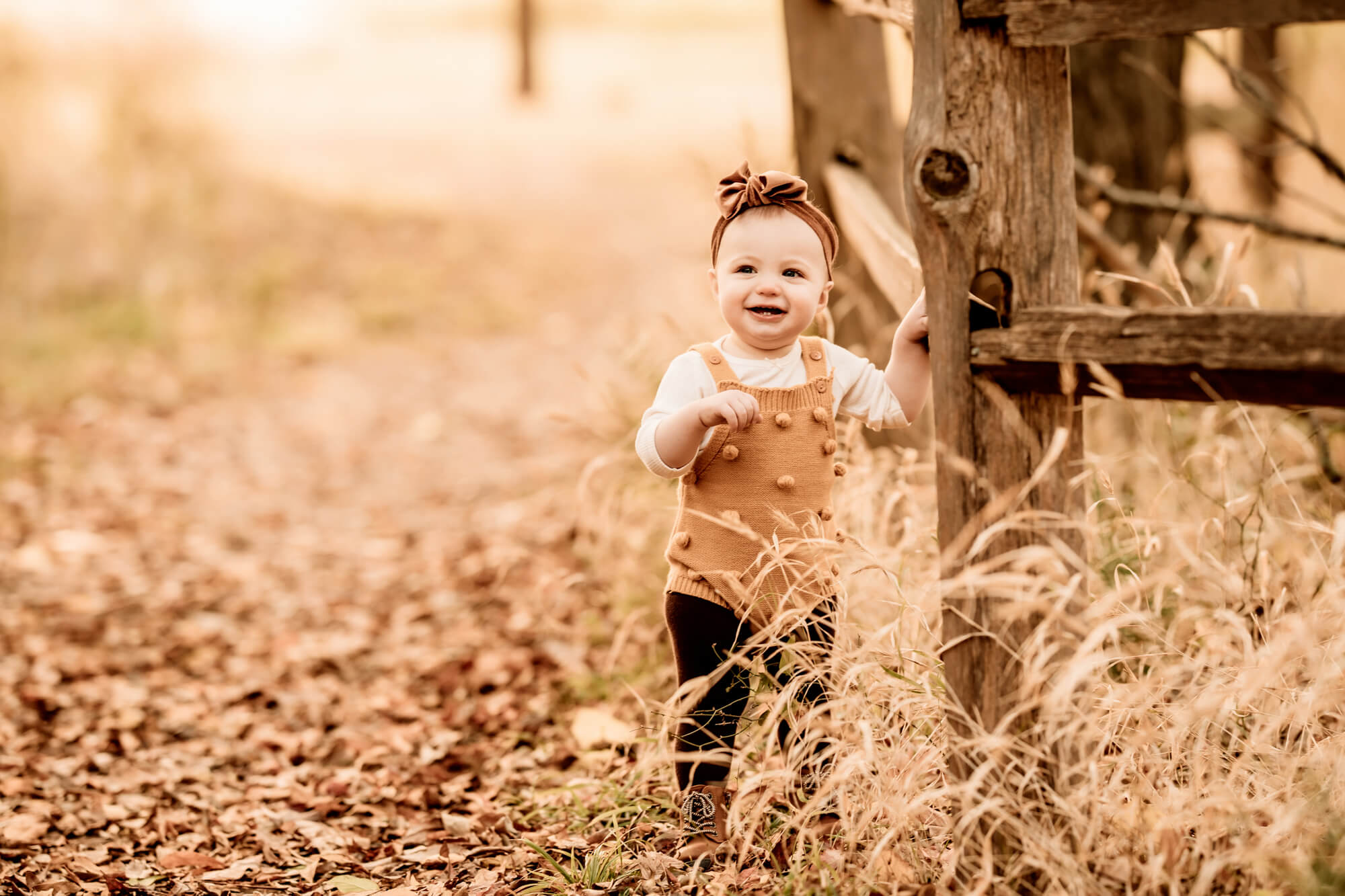 Girl with a yellow romper standing next to a fence in the fall, OKC pumpkin patch
