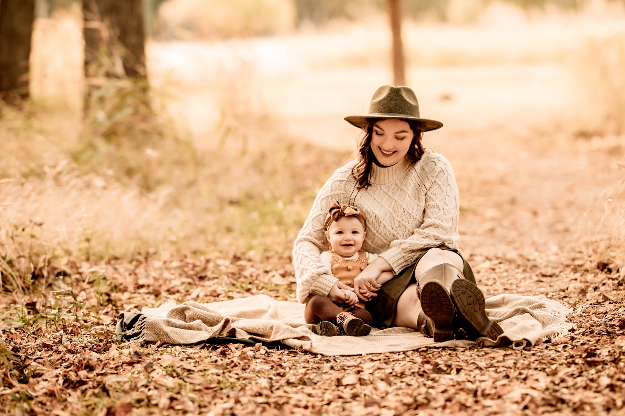 Mother and daughter sit together on a blanket with leave surrounding them, OKC pumpkin patch