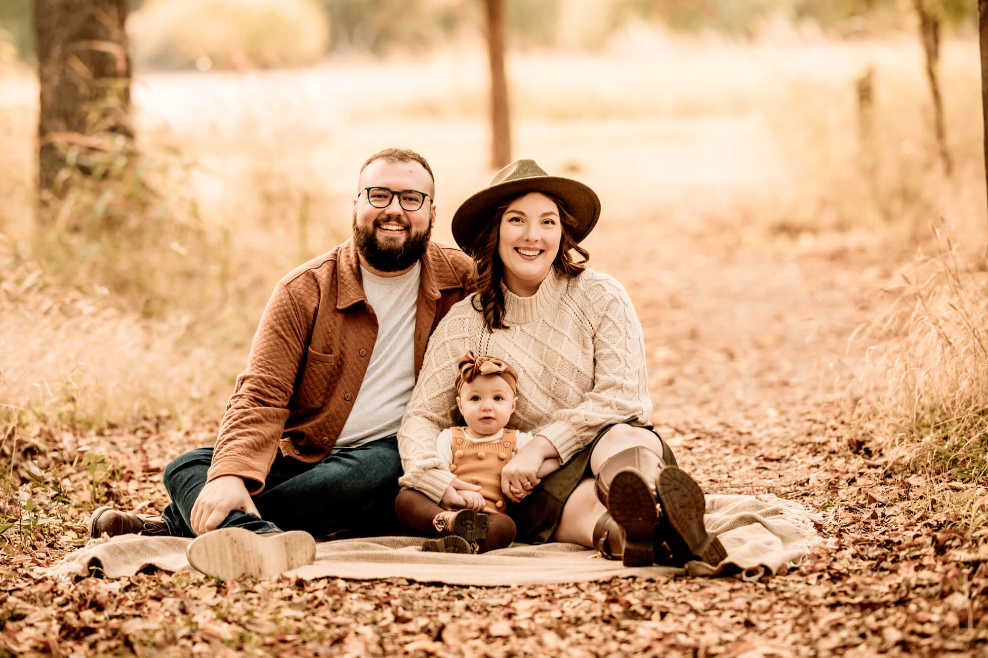 Family photo of a father, mother an done year old girl sitting on a blanket.